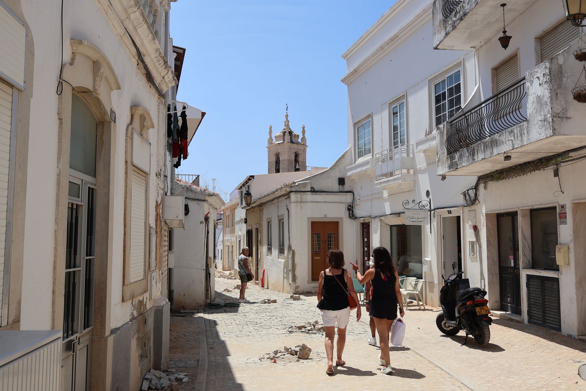 Dlážděná ulička historického města Tavira s bílými domy a kostelní věží na Algarve