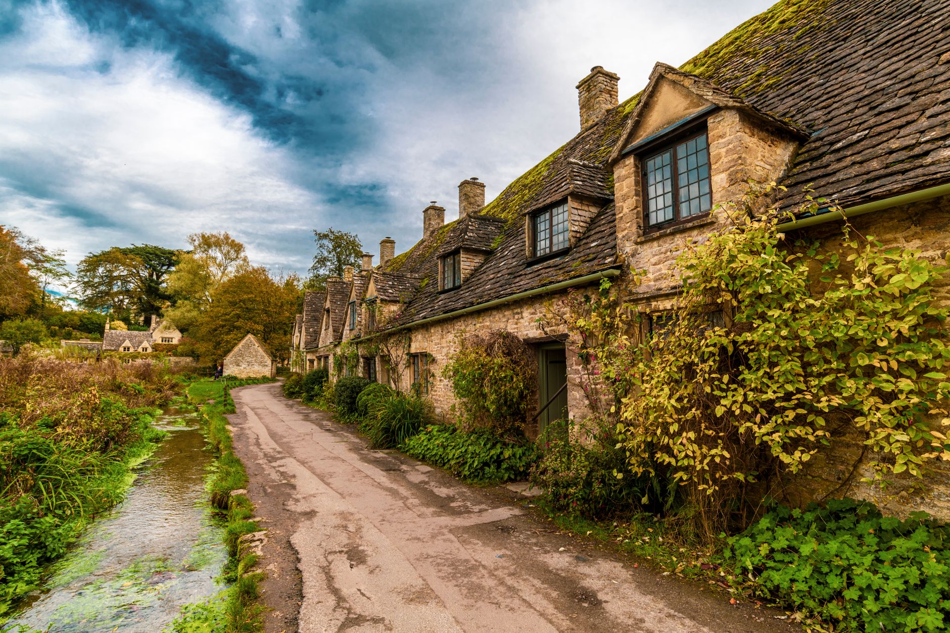 Vesnice z medově zlatého kamene s kamenným mostkem přes potok v anglickém venkově Cotswolds