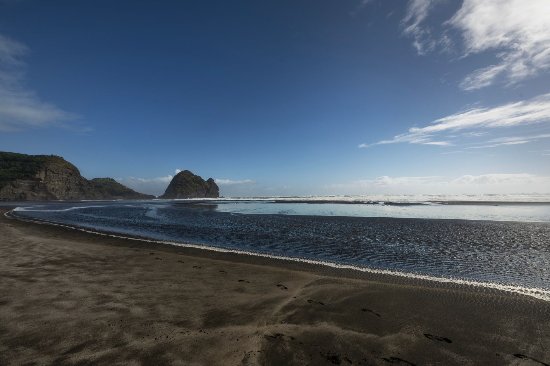 Černá sopečná pláž Piha s ostrohem Lion Rock západně od Aucklandu