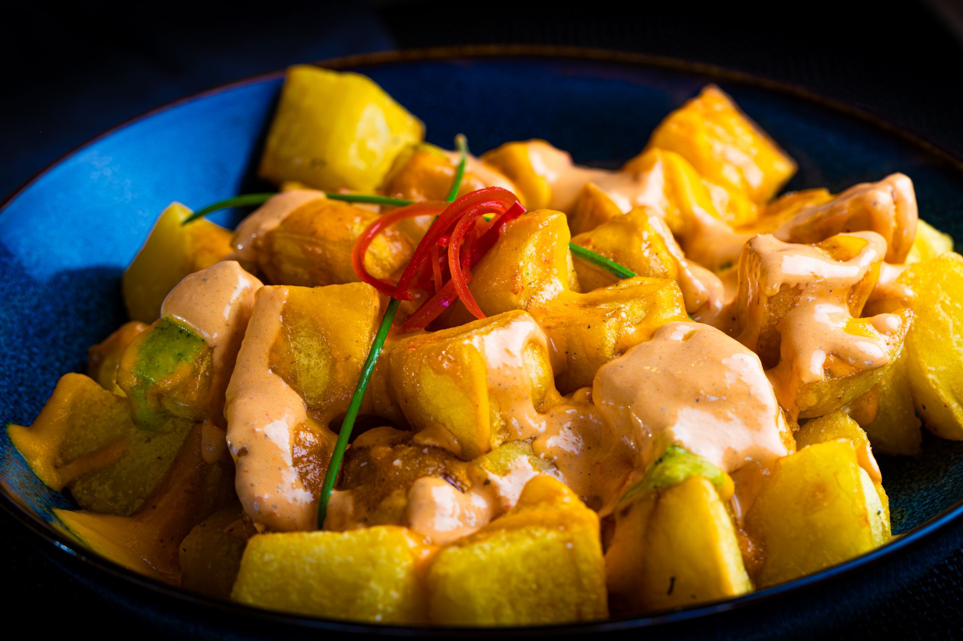 Talíř španělských tapas s patatas bravas a chlebem na stole v baru v Barceloně