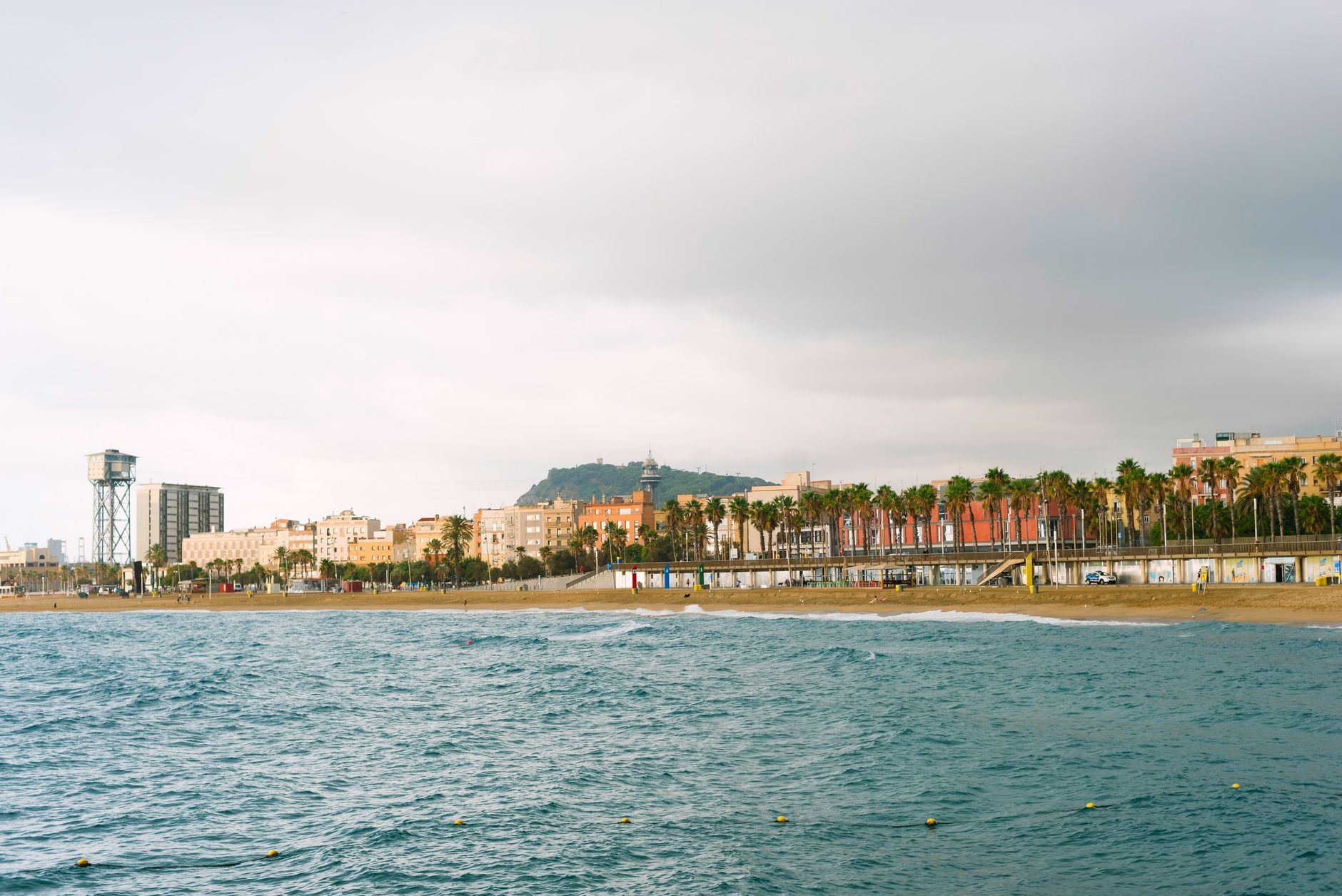 Pohled na barcelonskou pláž Barceloneta s pískem a mořem a panoramatem města
