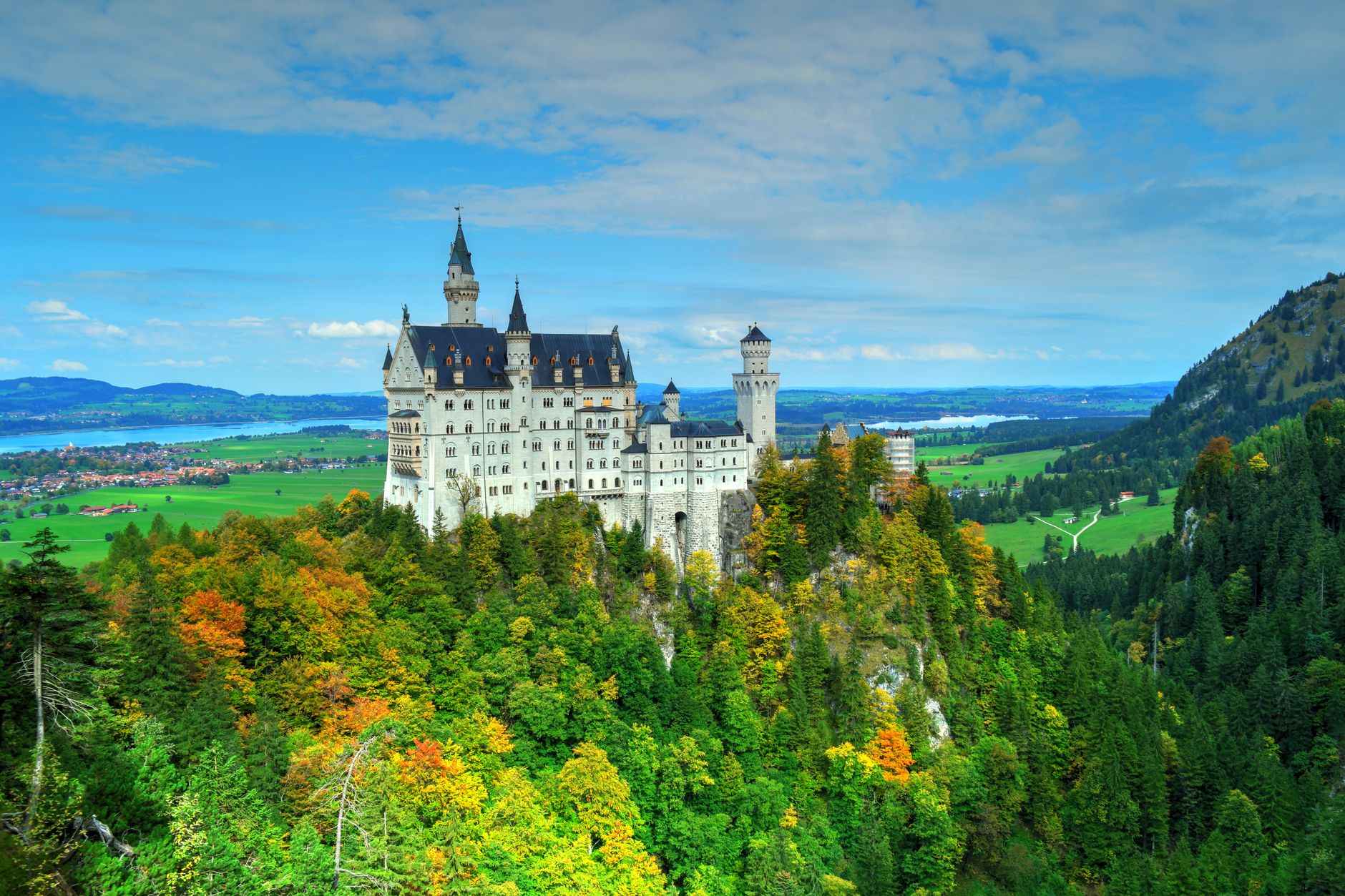 Pohádkový zámek Neuschwanstein na zalesněném kopci v bavorských Alpách s horami v pozadí