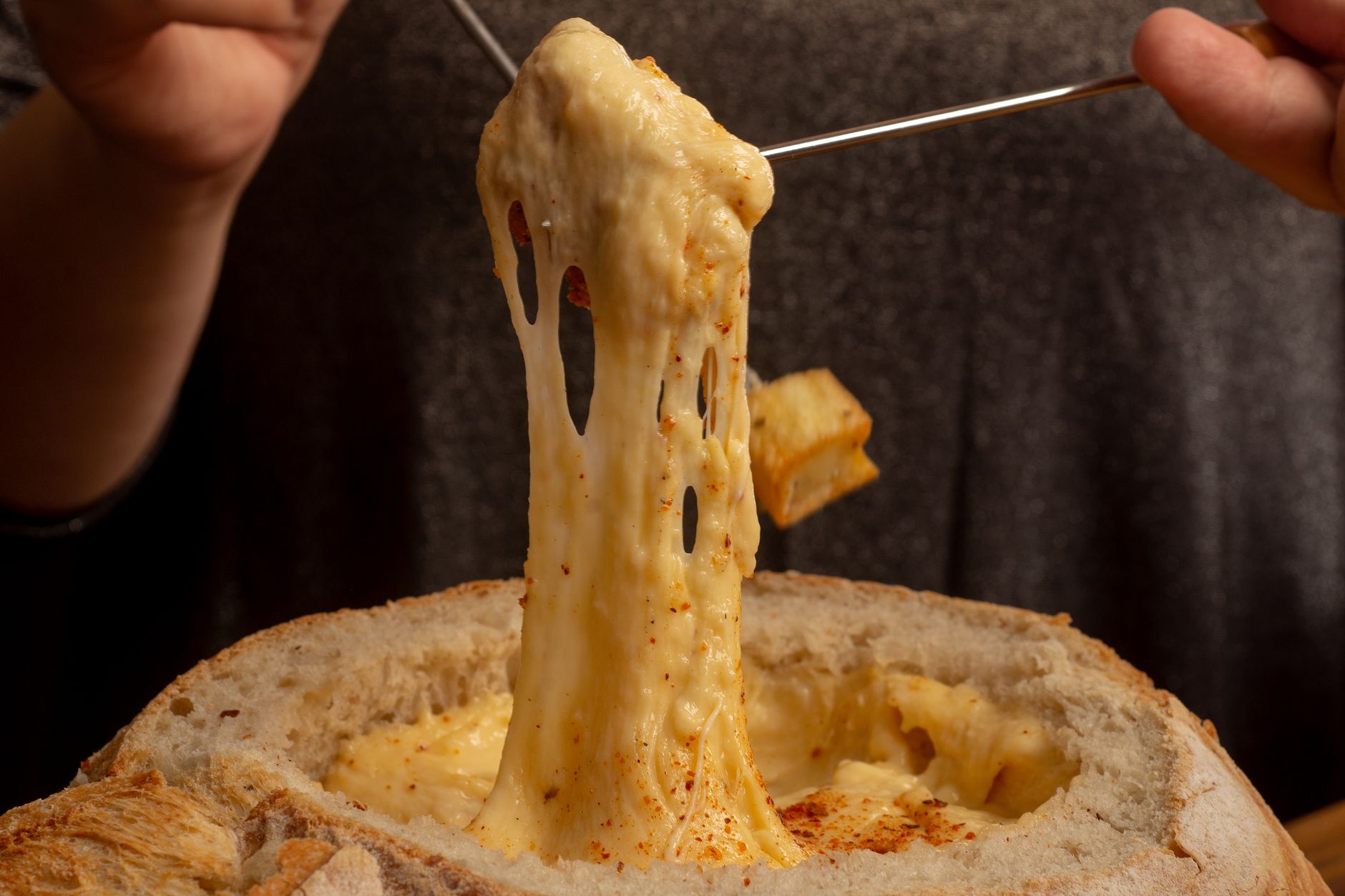 Švýcarské sýrové fondue v kotlíku nad ohřívačem s napíchnutým chlebem na vidličce