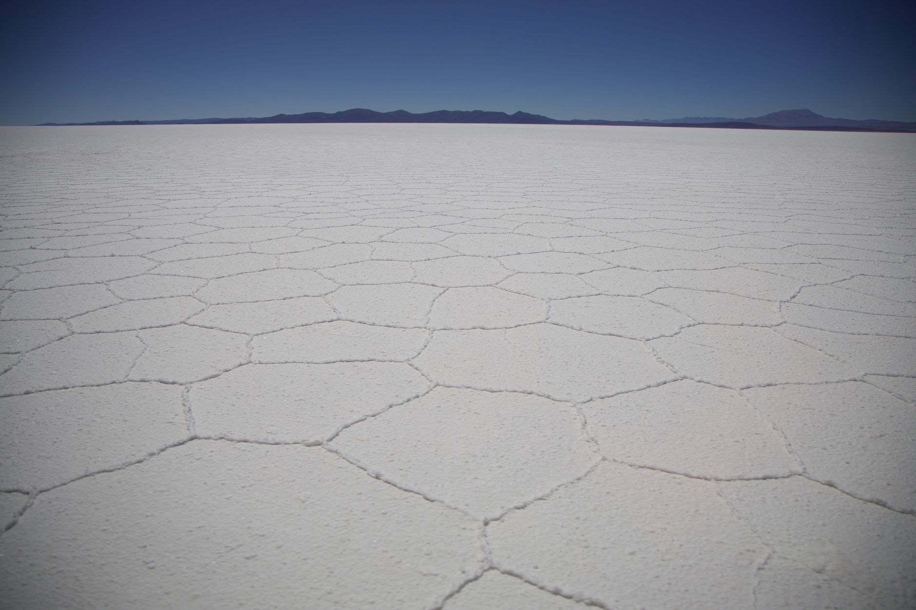 Solná pláň Salar de Uyuni v Bolívii s hexagonálními vzory soli sahajícími k horizontu pod modrou oblohou