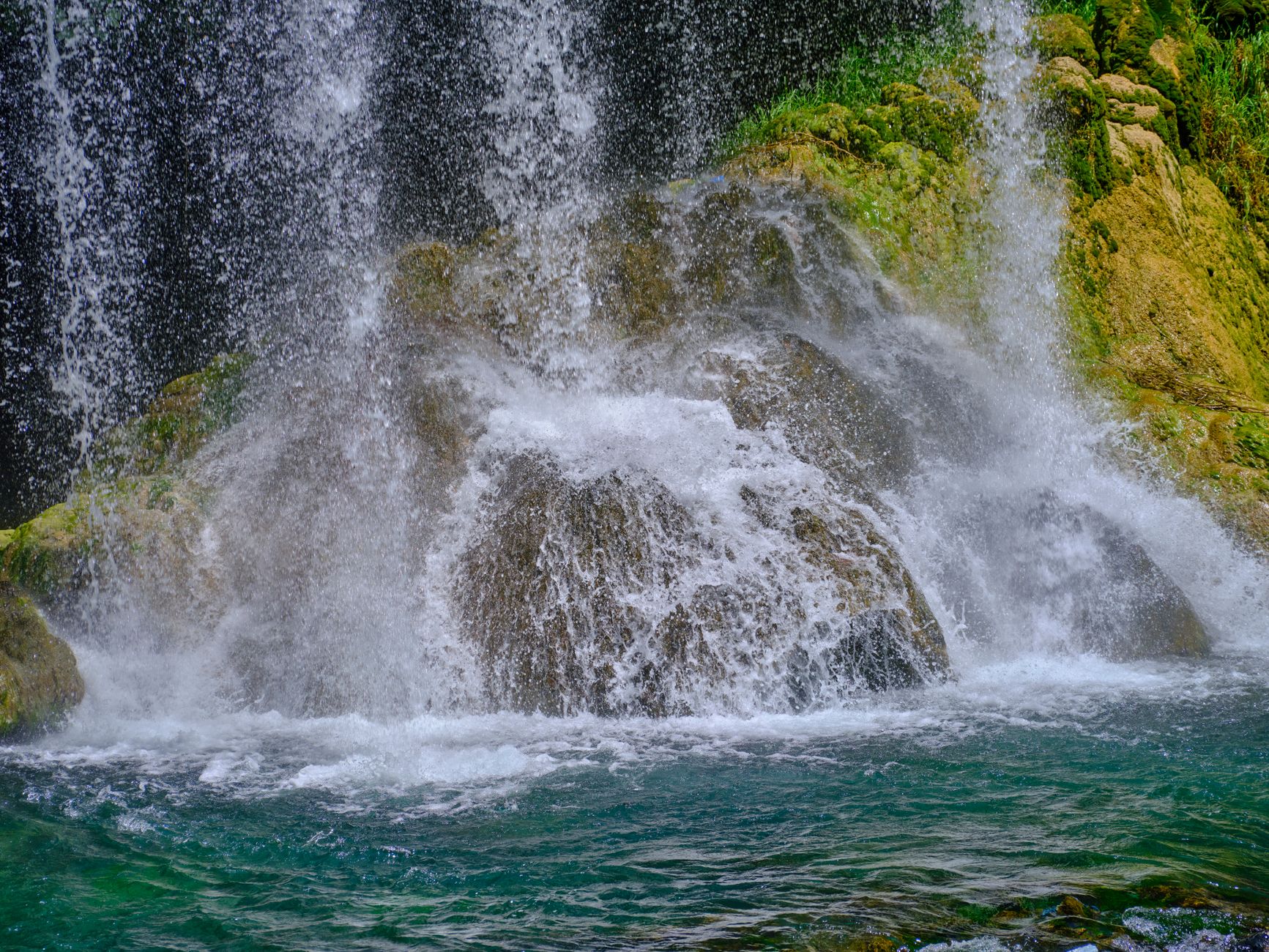 Široký půlkruh vodopádů Kravice padajících do tyrkysového jezírka obklopeného zelení