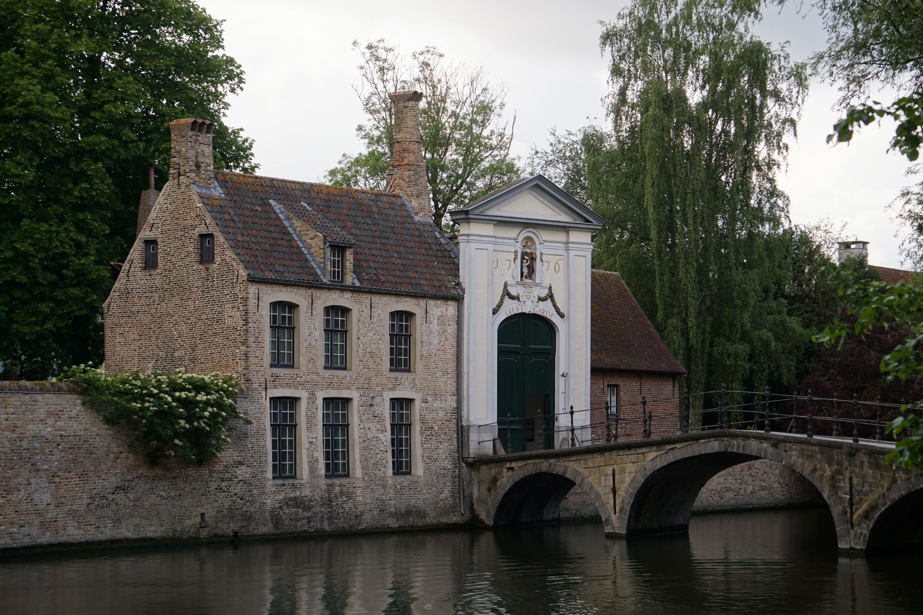 Pohled na kanál v Bruggách s historickými cihlovými domy a věží v pozadí