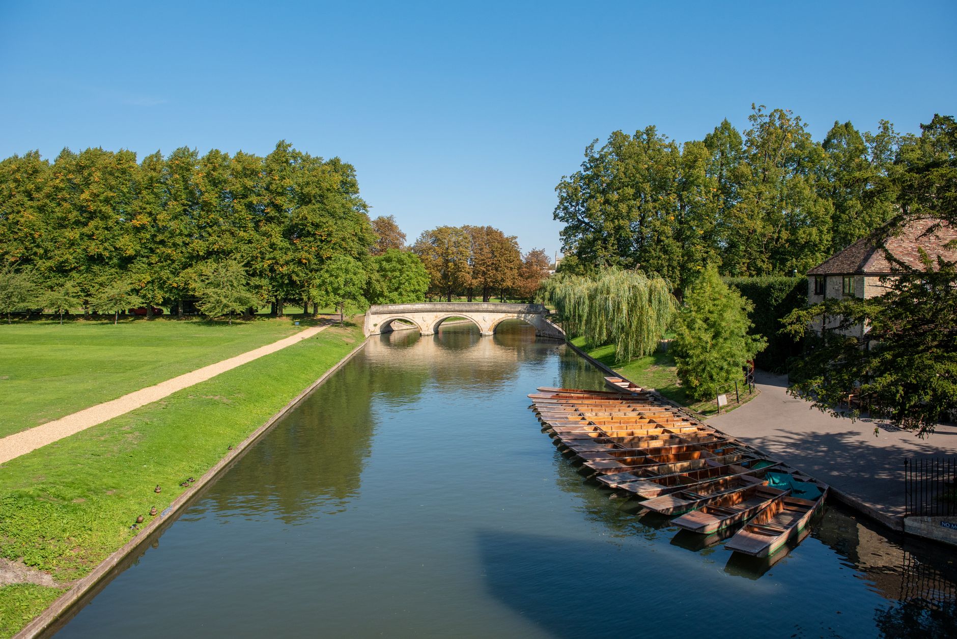 Ploché loďky pro punting kotvící u kamenného mostu na řece Cam v Cambridge