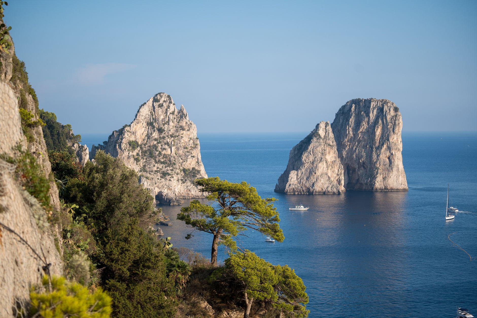 Tři skály Faraglioni vystupující z moře pohledem z vyhlídky v zahradách Giardini di Augusto na Capri