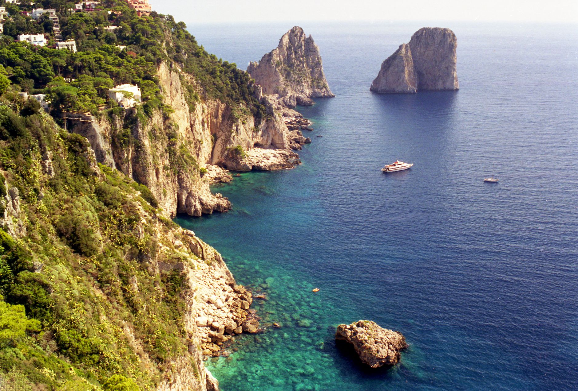 Skály Faraglioni vystupující z tyrkysového moře u pobřeží ostrova Capri za slunečného dne