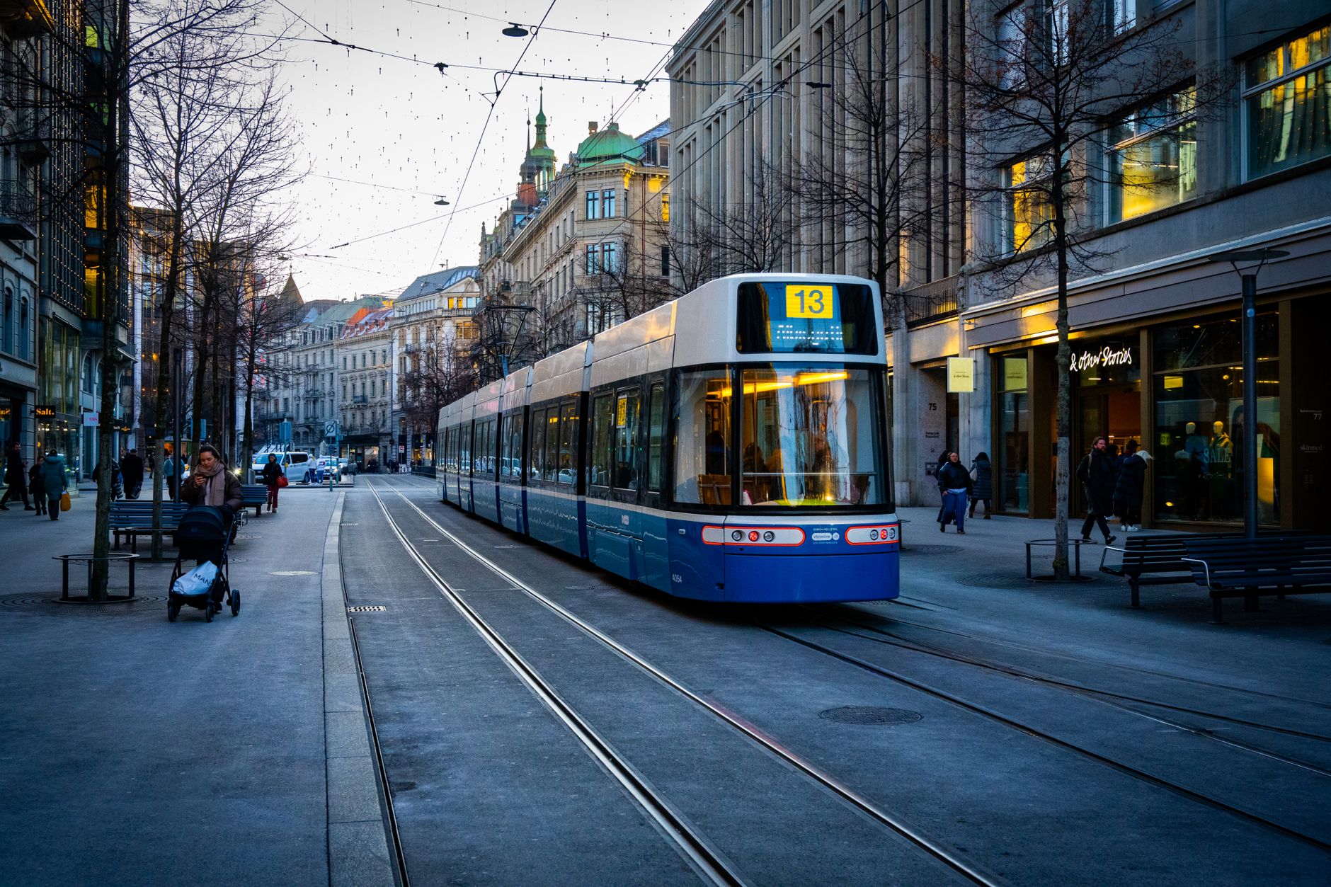 Modrá tramvaj projíždějící centrem Curychu kolem historických budov