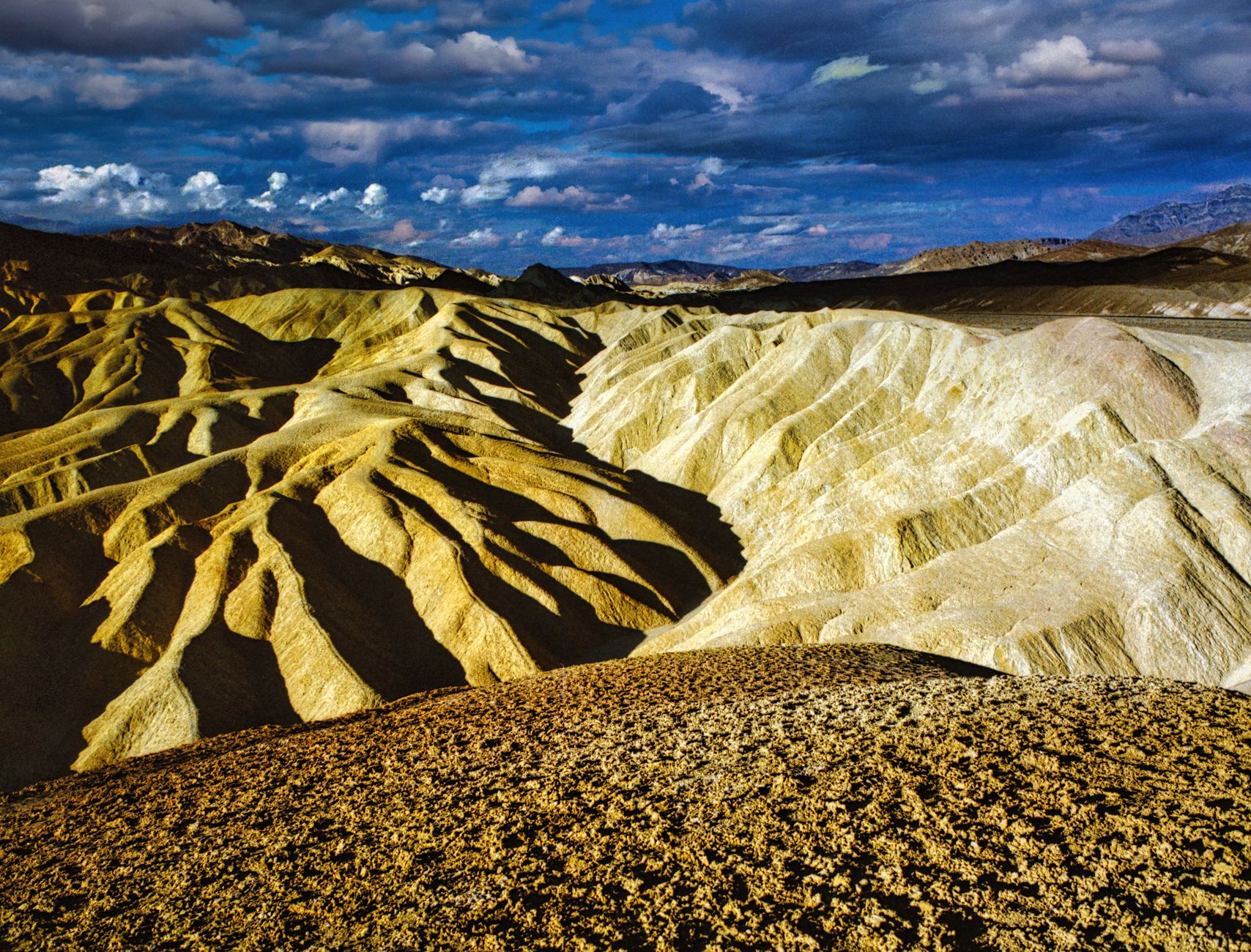 Zvlněné žluté a hnědé hřebeny pustiny z vyhlídky Zabriskie Point v Death Valley