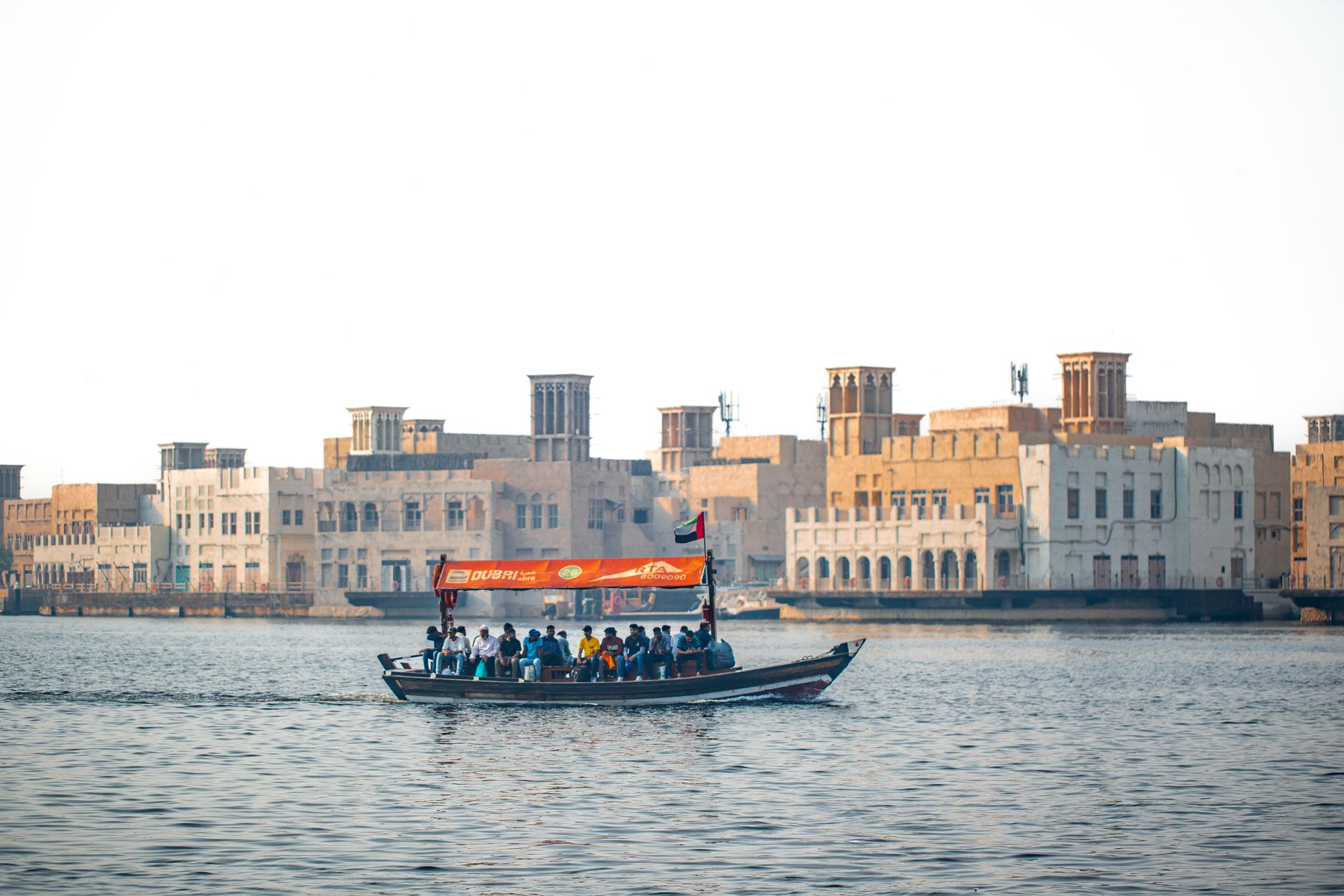 Tradiční dřevěná loďka abra na vodě Dubai Creek se starou čtvrtí v pozadí