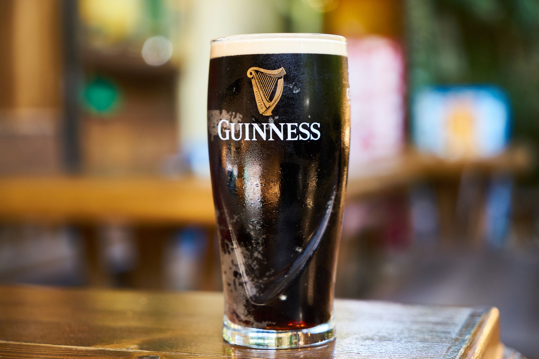 Čerstvě načepovaná pinta tmavého piva Guinness s krémovou pěnou na dřevěném stole v irské hospodě