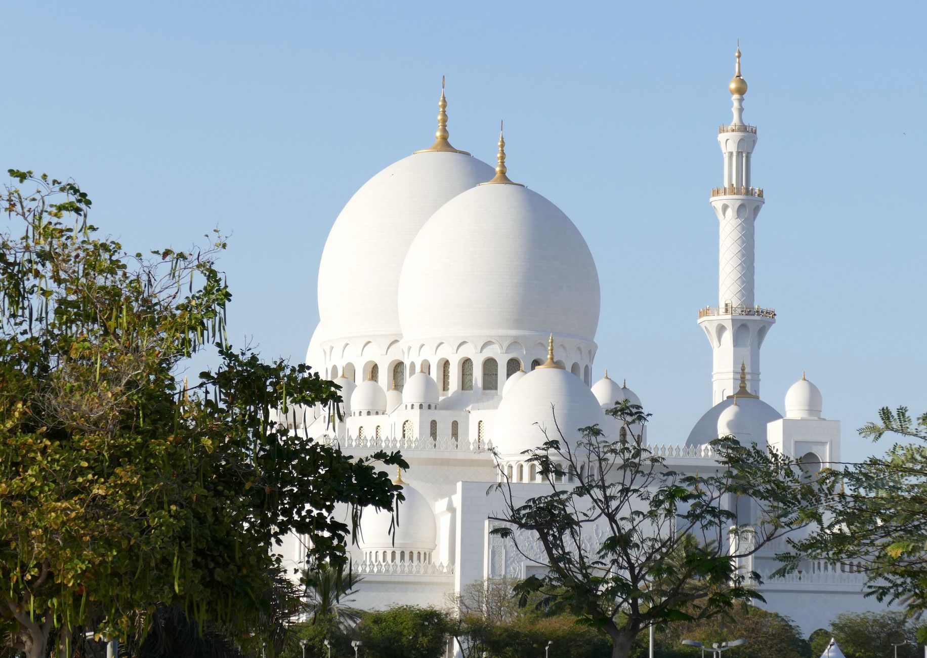 Bílá Velká mešita šejka Zájda v Abú Dhabí s kopulemi a minarety odrážející se ve vodní hladině