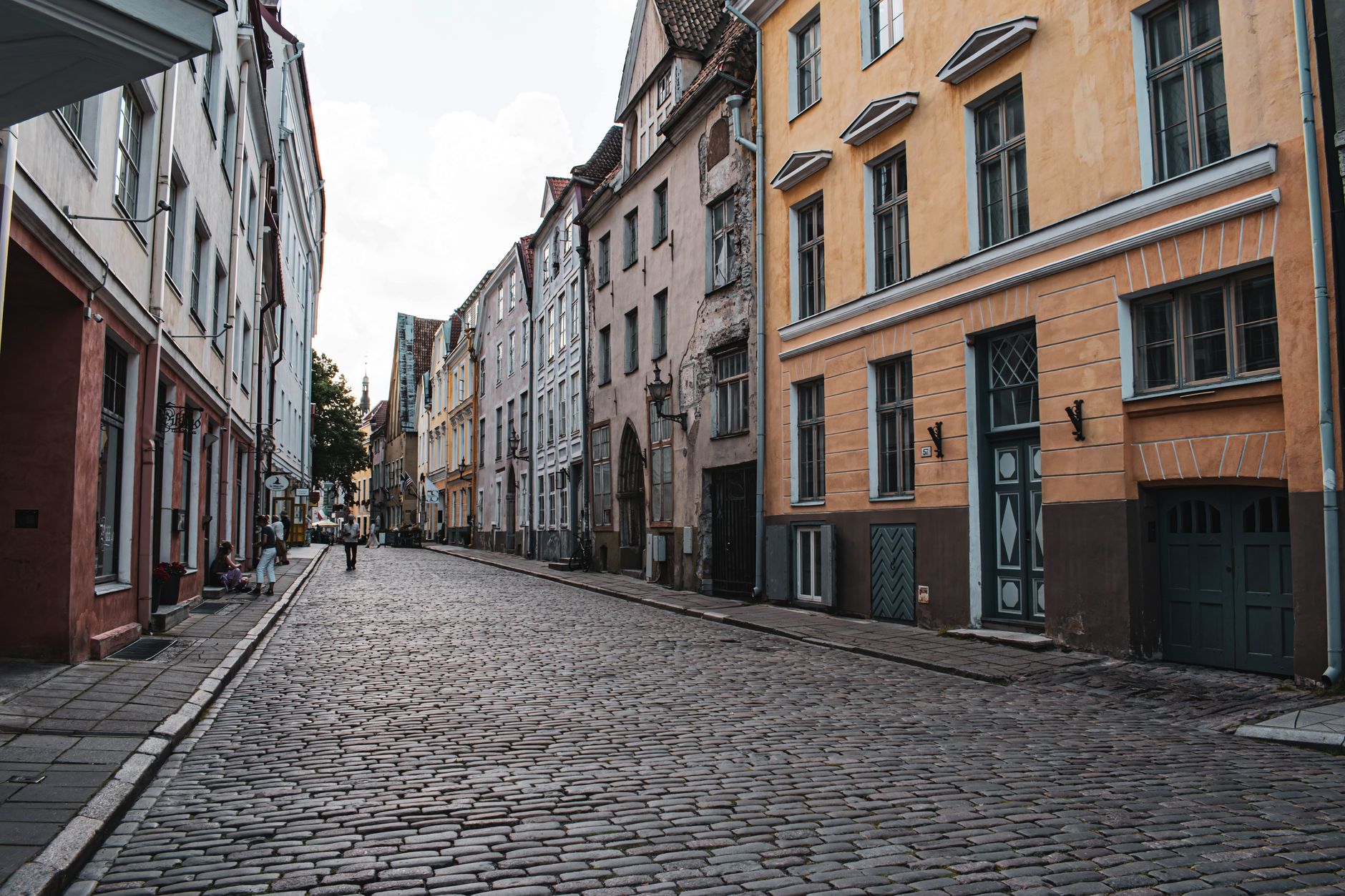 Dlážděná ulička starého města Tallinnu s historickými kupeckými domy a kostelní věží v pozadí