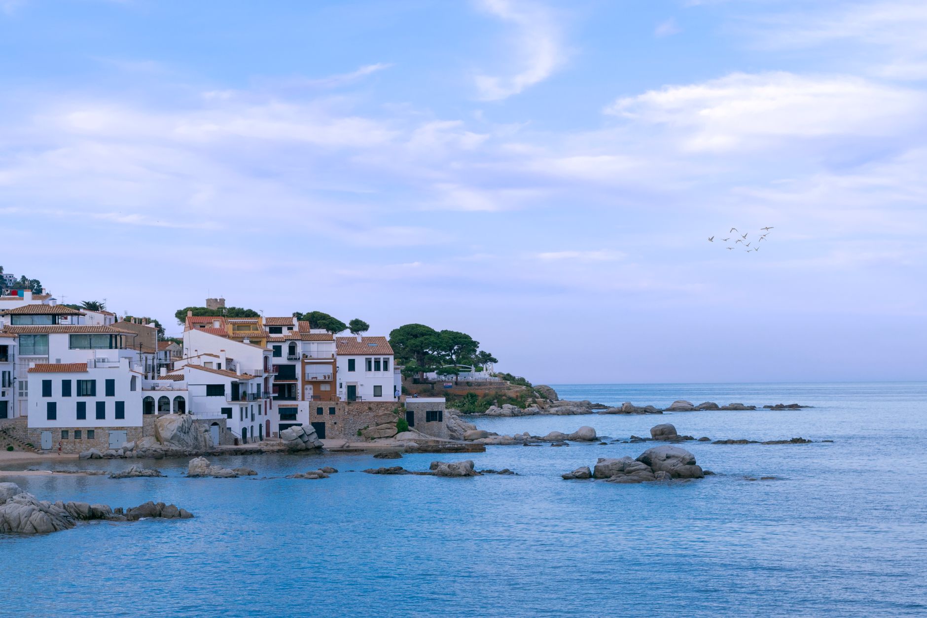 Bílé domy s modrými okenicemi nad kamennou zátokou ve městečku Cadaqués na pobřeží Costa Brava