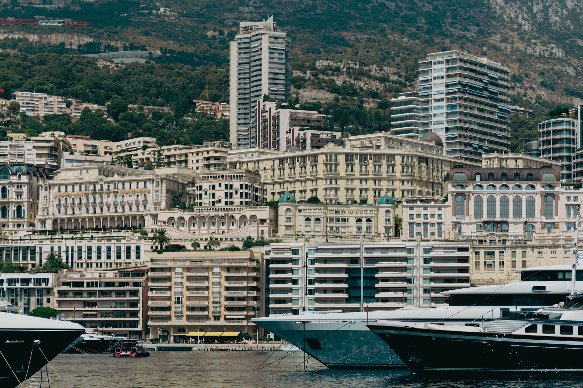 Přístav v Monaku Port Hercule plný luxusních jachet pod kopcem se zástavbou