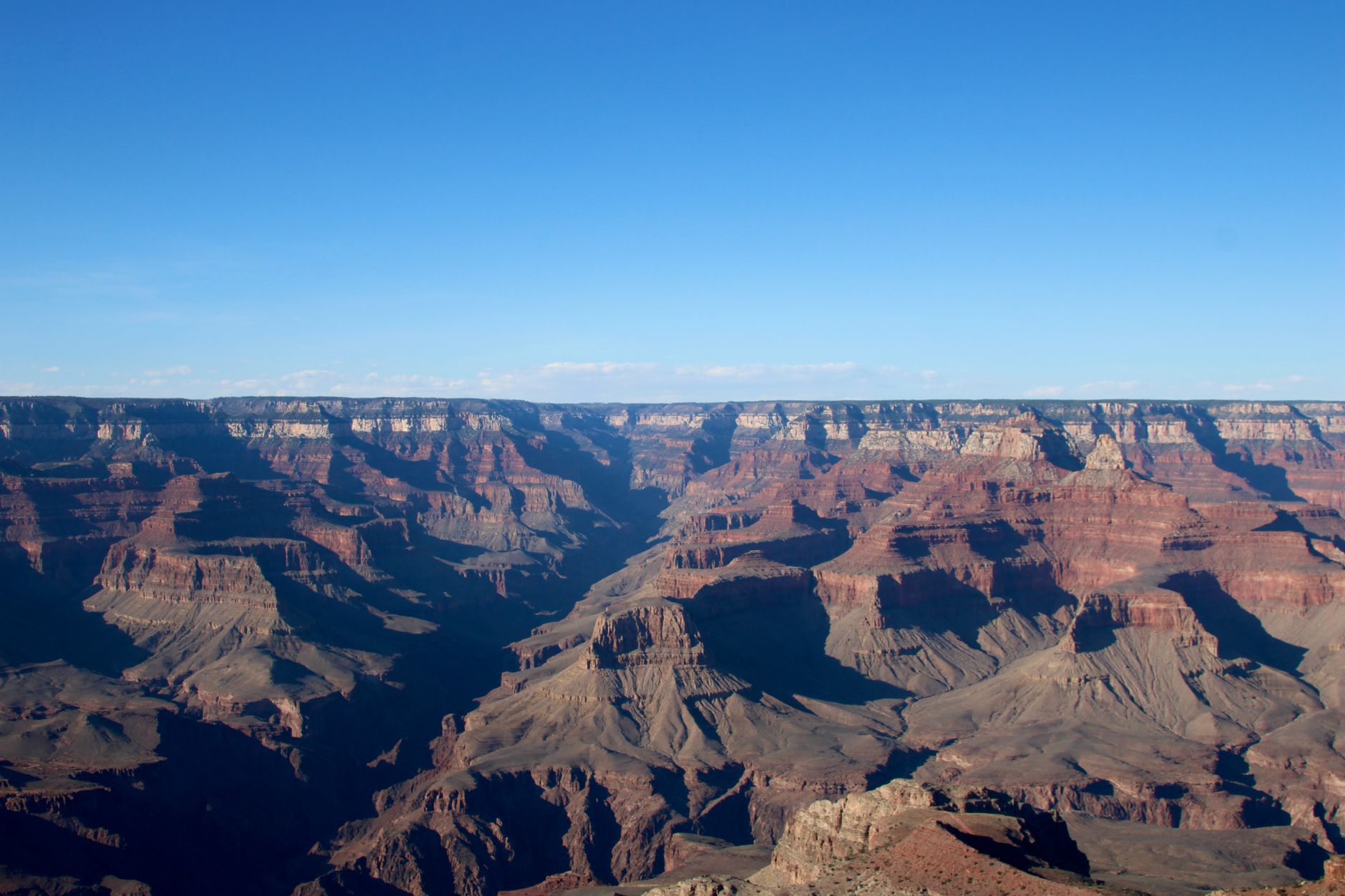Vrstevnaté červené a oranžové skalní útvary Grand Canyonu pod modrou oblohou z jižního okraje