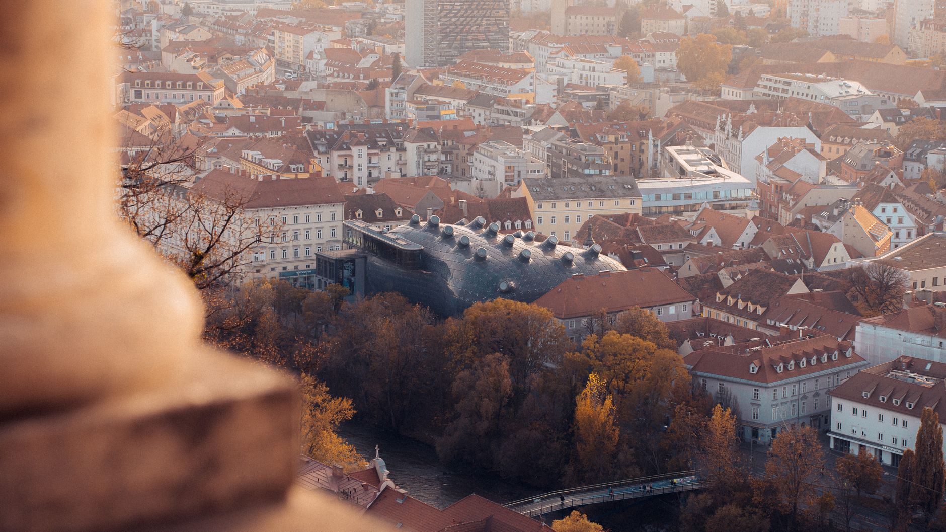 Moderní biomorfní stavba Kunsthaus Graz s modrým pláštěm vedle historických domů u řeky Mur