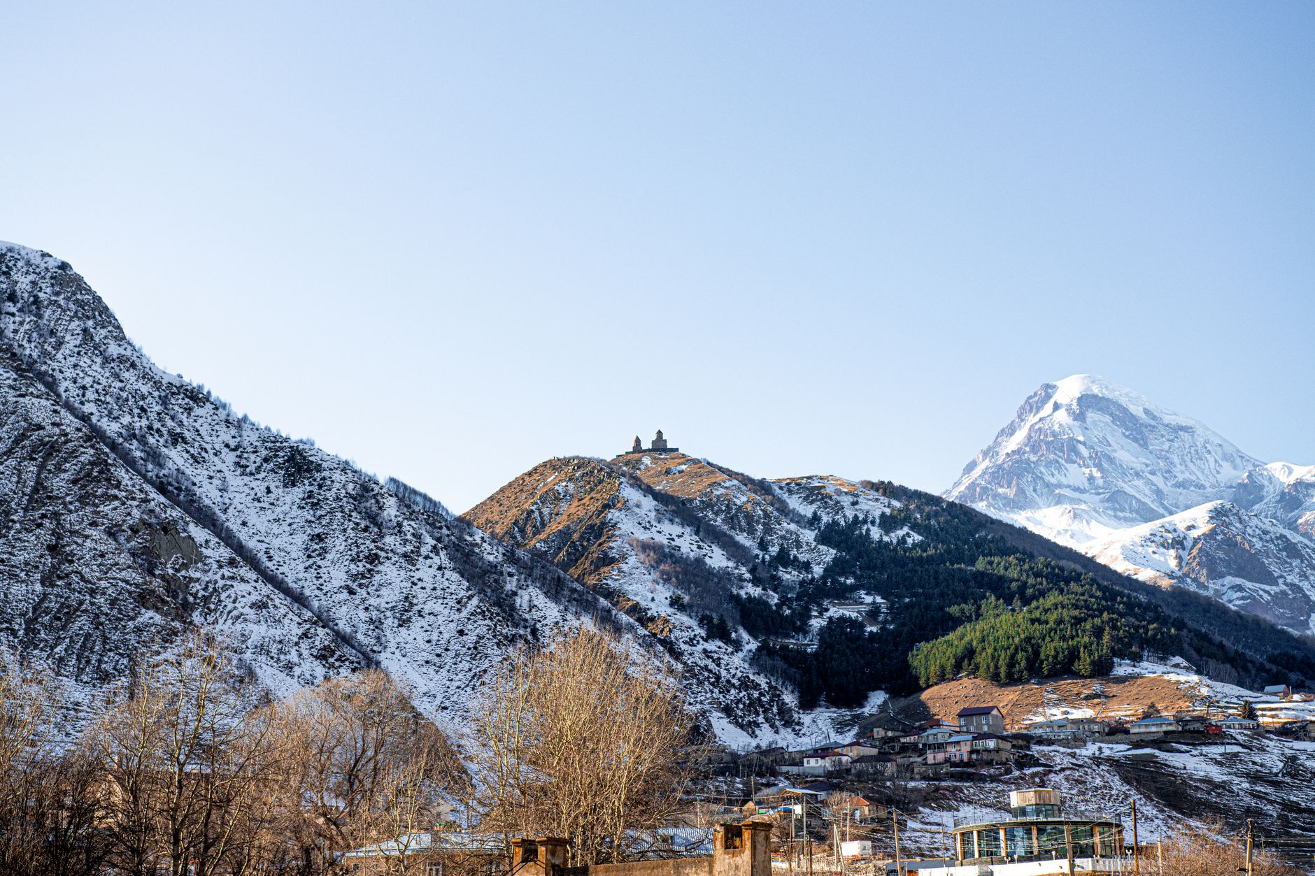 Kostel Gergeti Trinity na zeleném kopci pod zasněženým vrcholem Kazbek v gruzínském Kavkazu