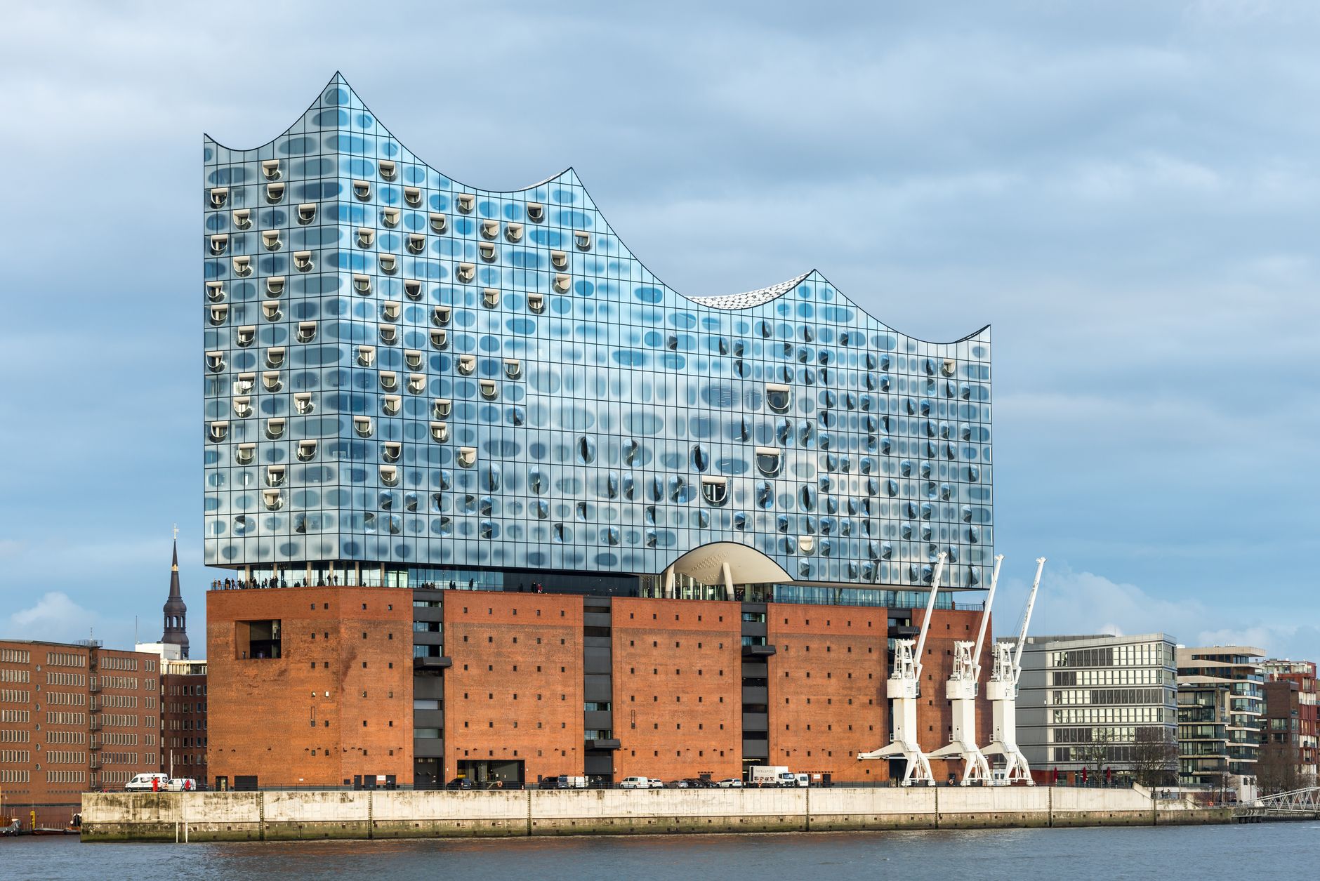 Skleněná zvlněná střecha Labské filharmonie nad cihlovou základnou v hamburské čtvrti HafenCity