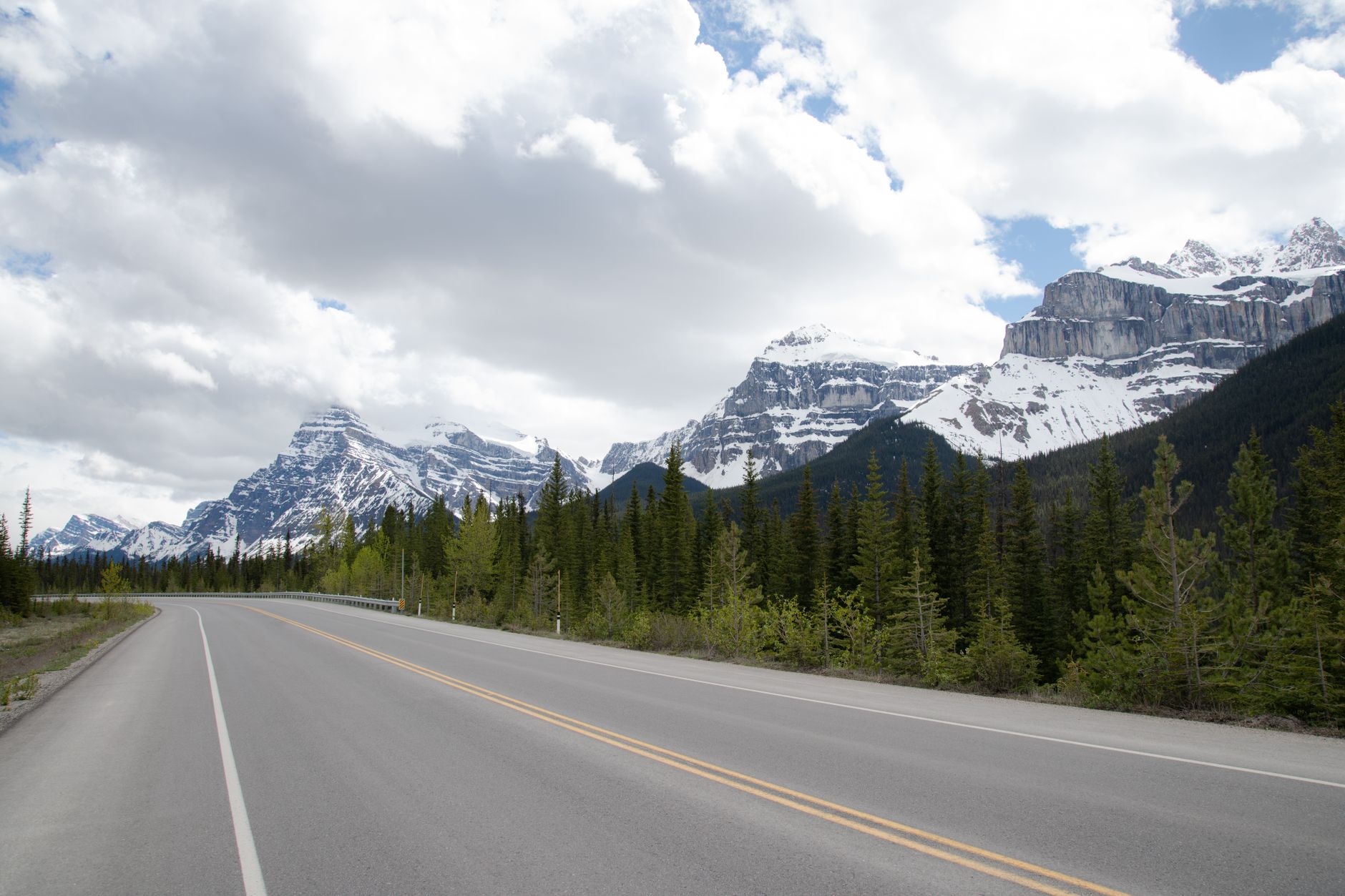 Vyhlídková horská silnice Icefields Parkway ve Skalnatých horách lemovaná jehličnatým lesem a zasněženými štíty