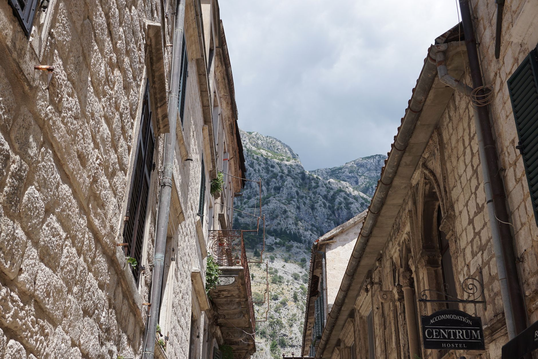 Úzká kamenná ulička ve starém městě Kotor s kostelní věží a okenicemi
