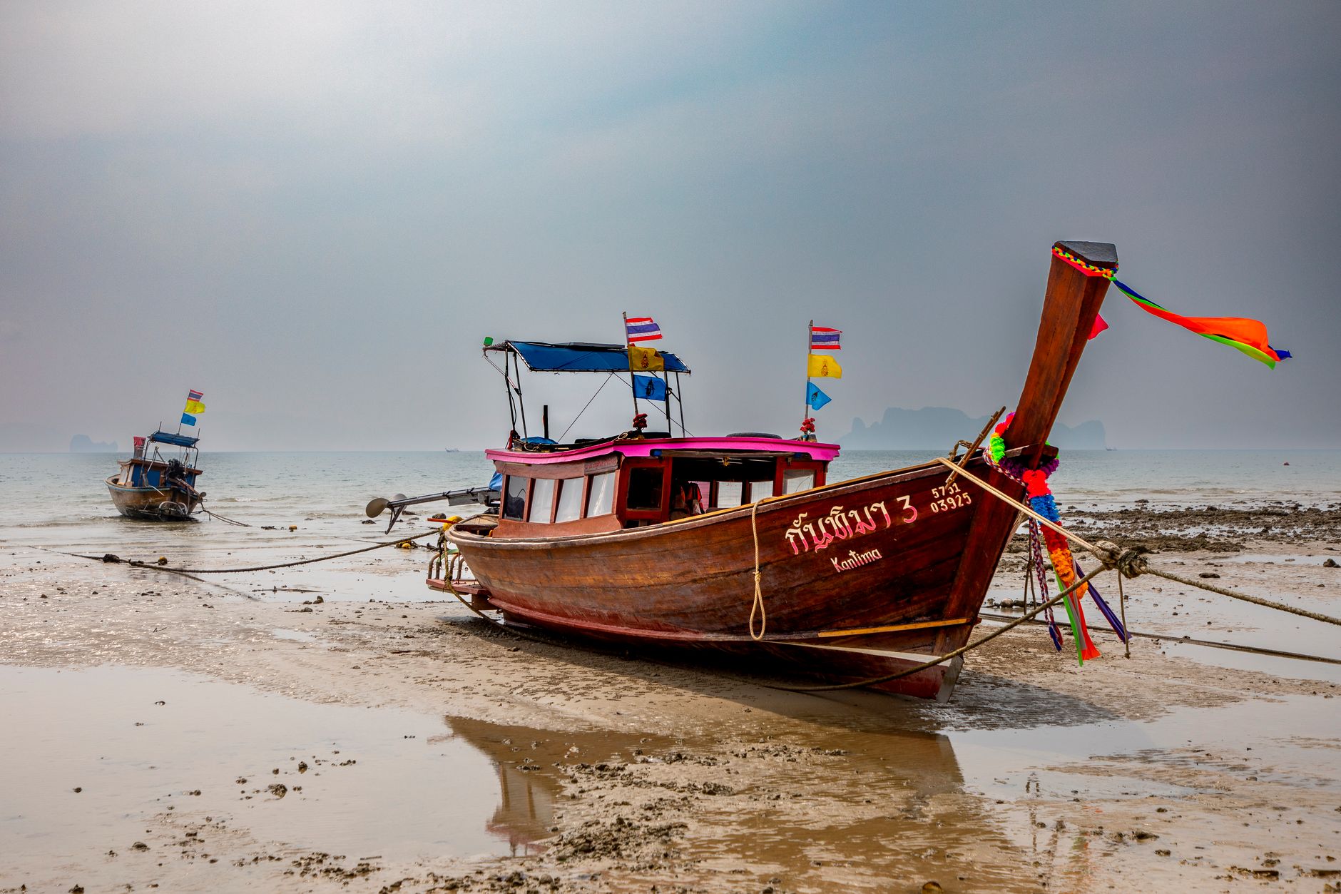 Dřevěné longtail lodě s barevnými stuhami u břehu pláže v Krabi