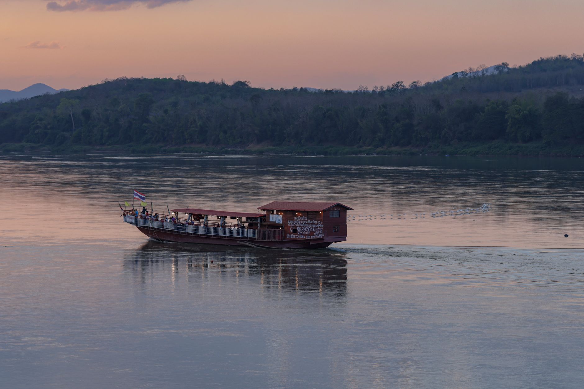 Dřevěné pomalé čluny kotvící na hnědé hladině řeky Mekong v Laosu za úsvitu