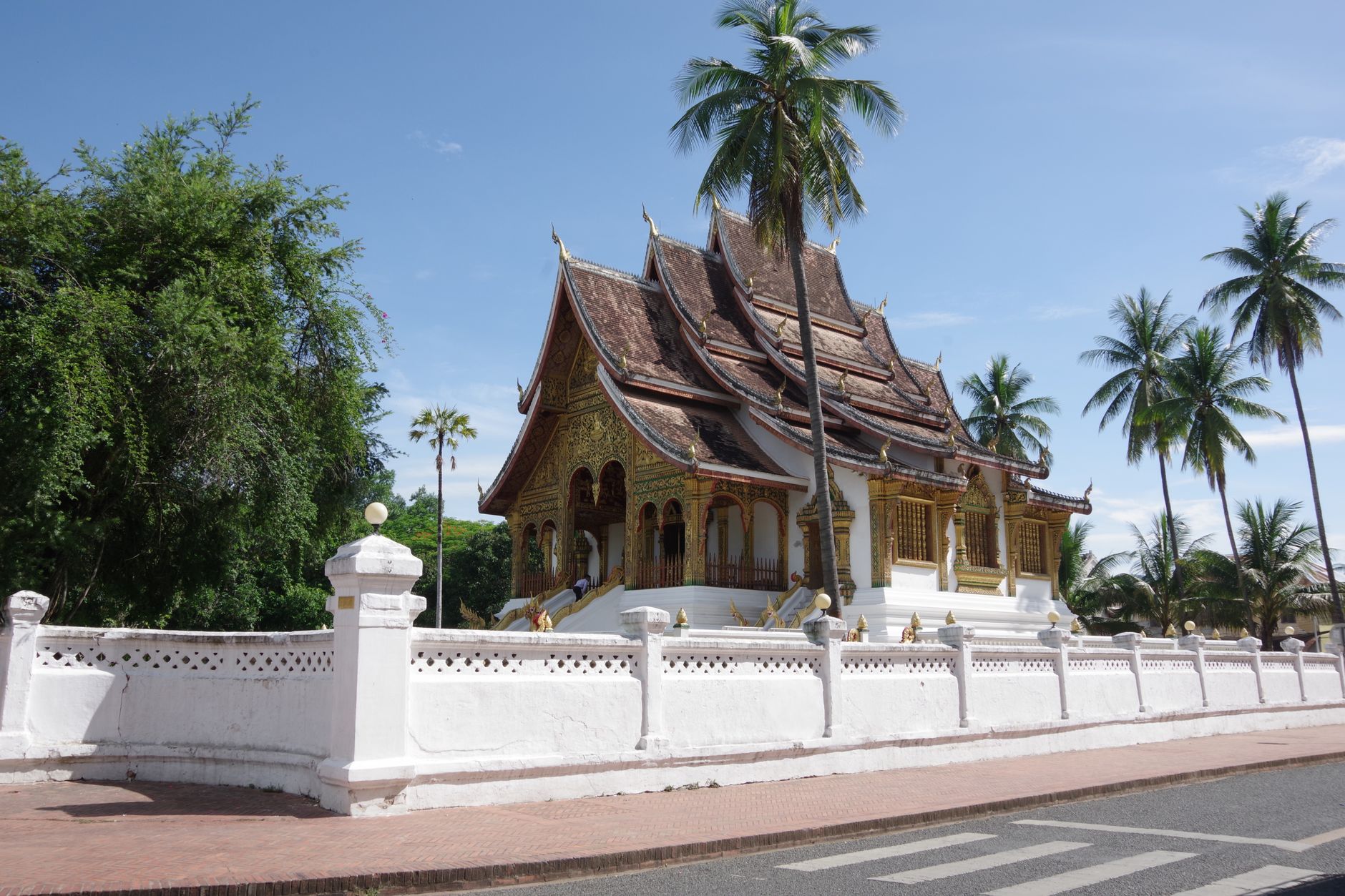 Pozlacený chrám Wat Xieng Thong v Luang Prabangu s vícevrstvou střechou a palmami v pozadí