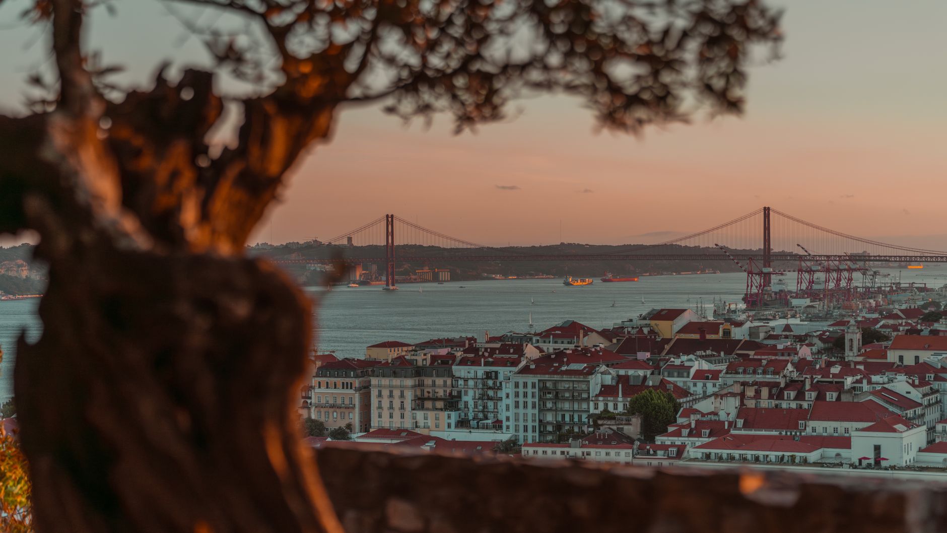 Panorama Lisabonu s červenými střechami, řekou Tejo a hradem São Jorge nad městem za soumraku