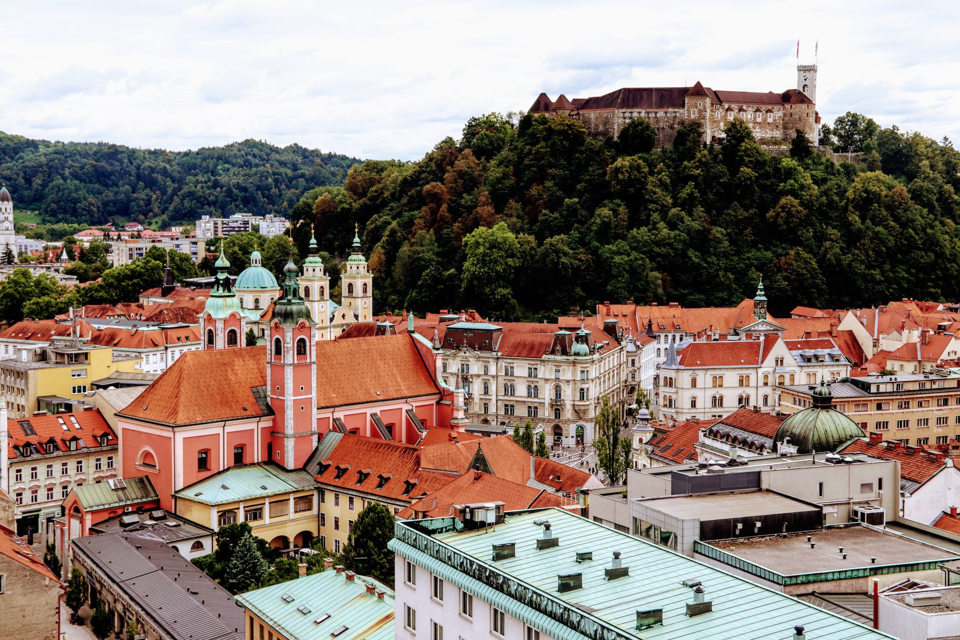 Lublaňský hrad na zalesněném kopci nad červenými střechami starého města