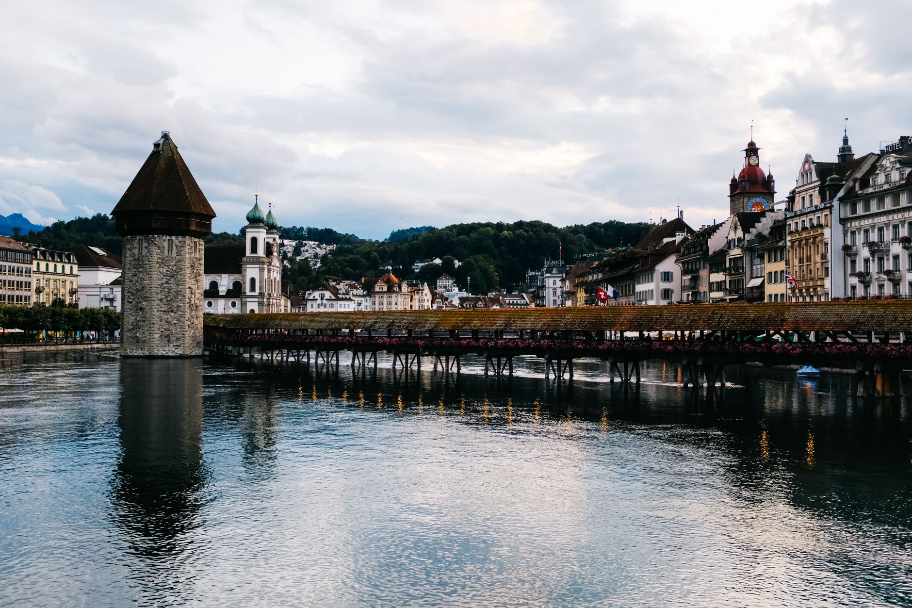 Dřevěný most Kapellbrücke s osmibokou věží Wasserturm přes řeku Reuss v Luzernu a hory v pozadí