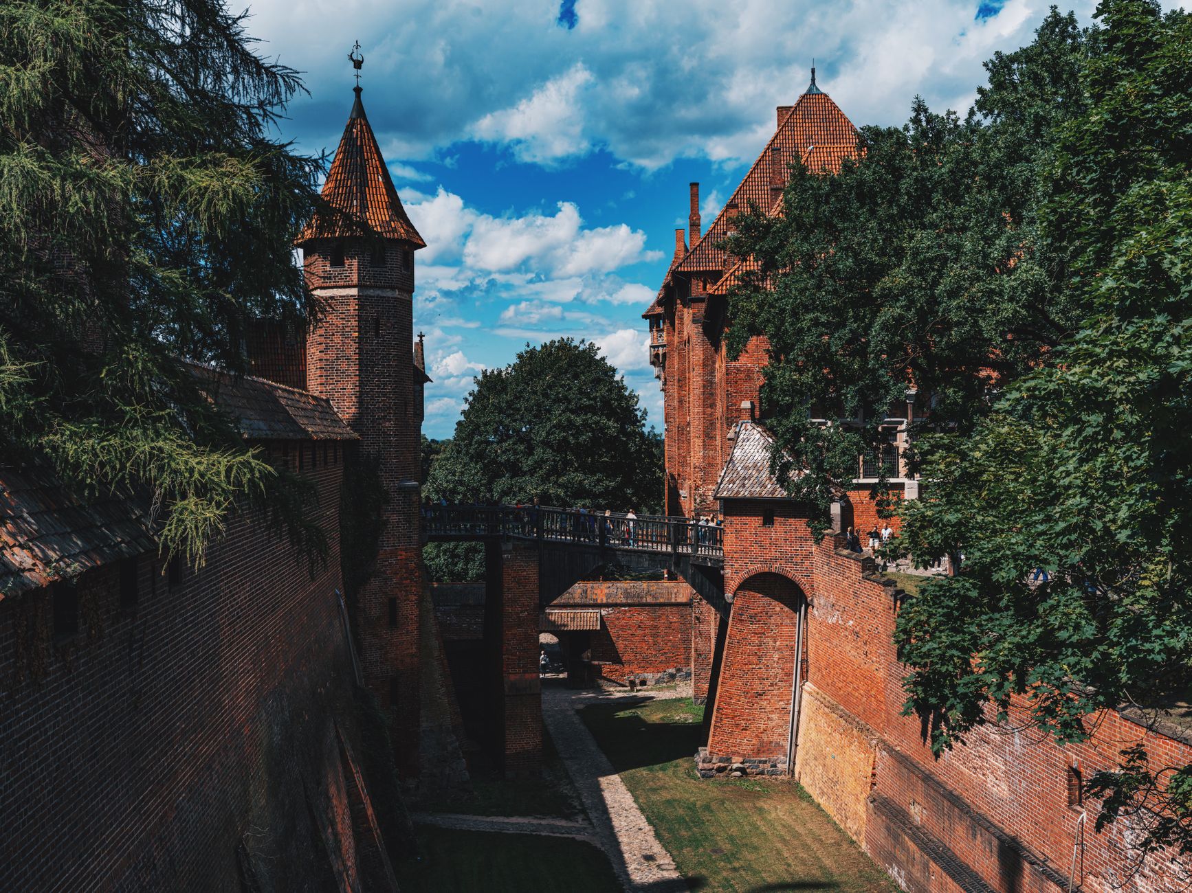 Cihlový hrad Malbork odrážející se v hladině řeky Nogat za jasného dne