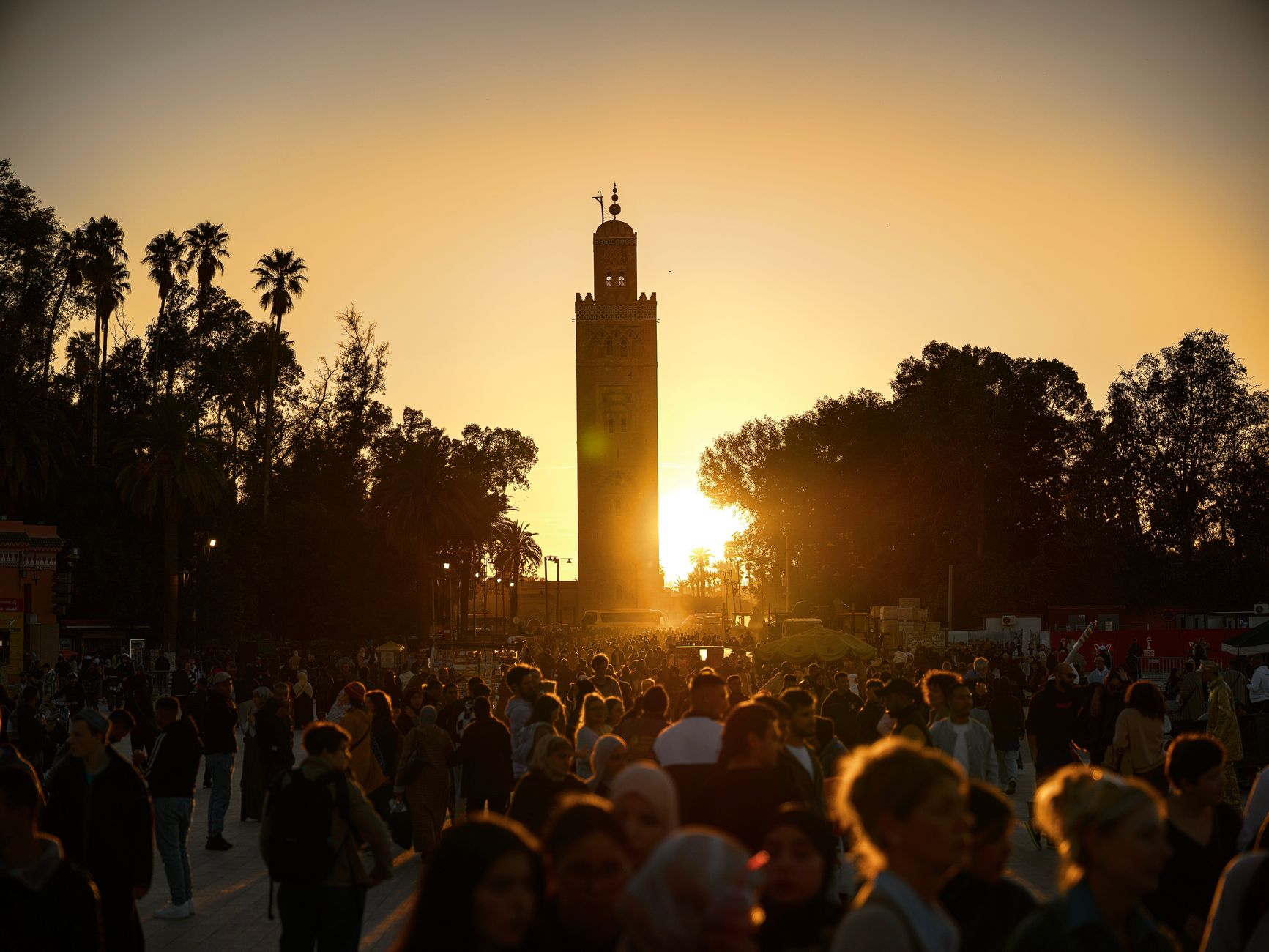 Minaret mešity Koutoubia nad střechami Marrákeše s pohořím Atlas v pozadí za soumraku