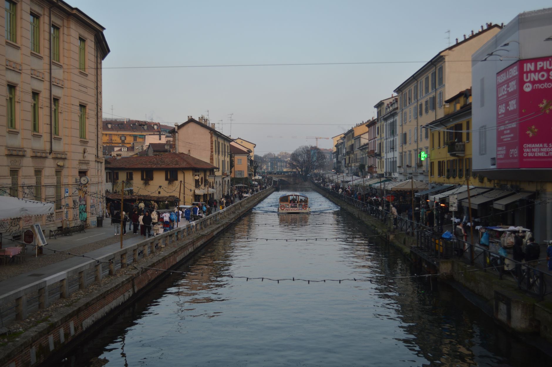 Kanál ve čtvrti Navigli v Miláně s restauračními terasami a odrazy ve vodě za soumraku