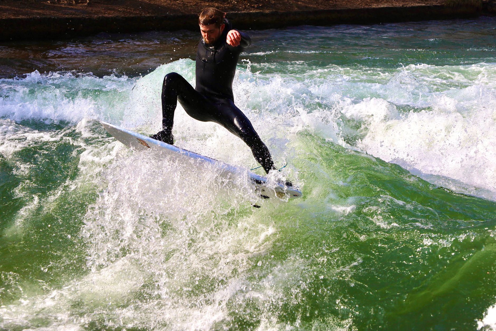 Surfař na vlně Eisbach v Anglické zahradě v centru Mnichova obklopený zelení