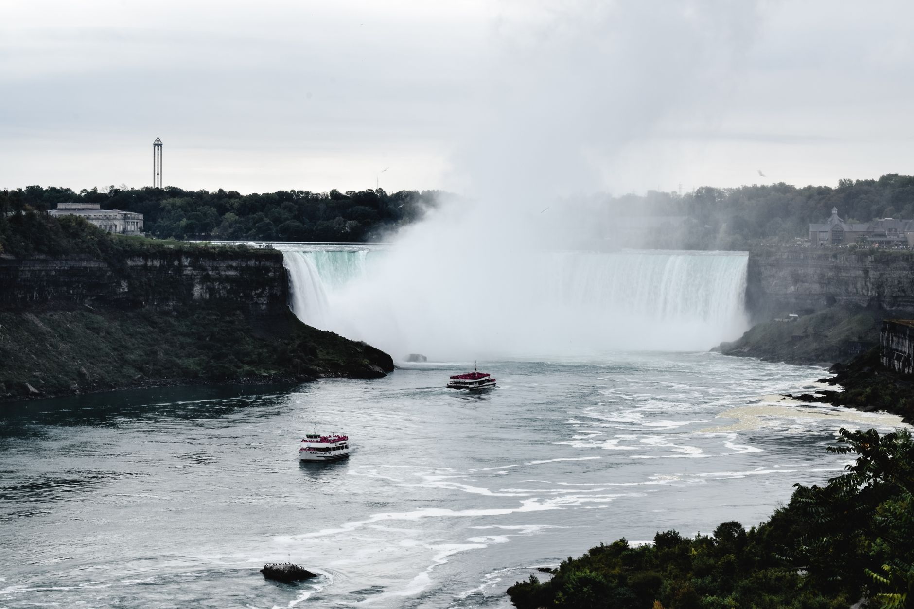 Výletní loď plující po hladině řeky Niagara těsně pod hřmícím Horseshoe Falls v oblaku vodní tříště