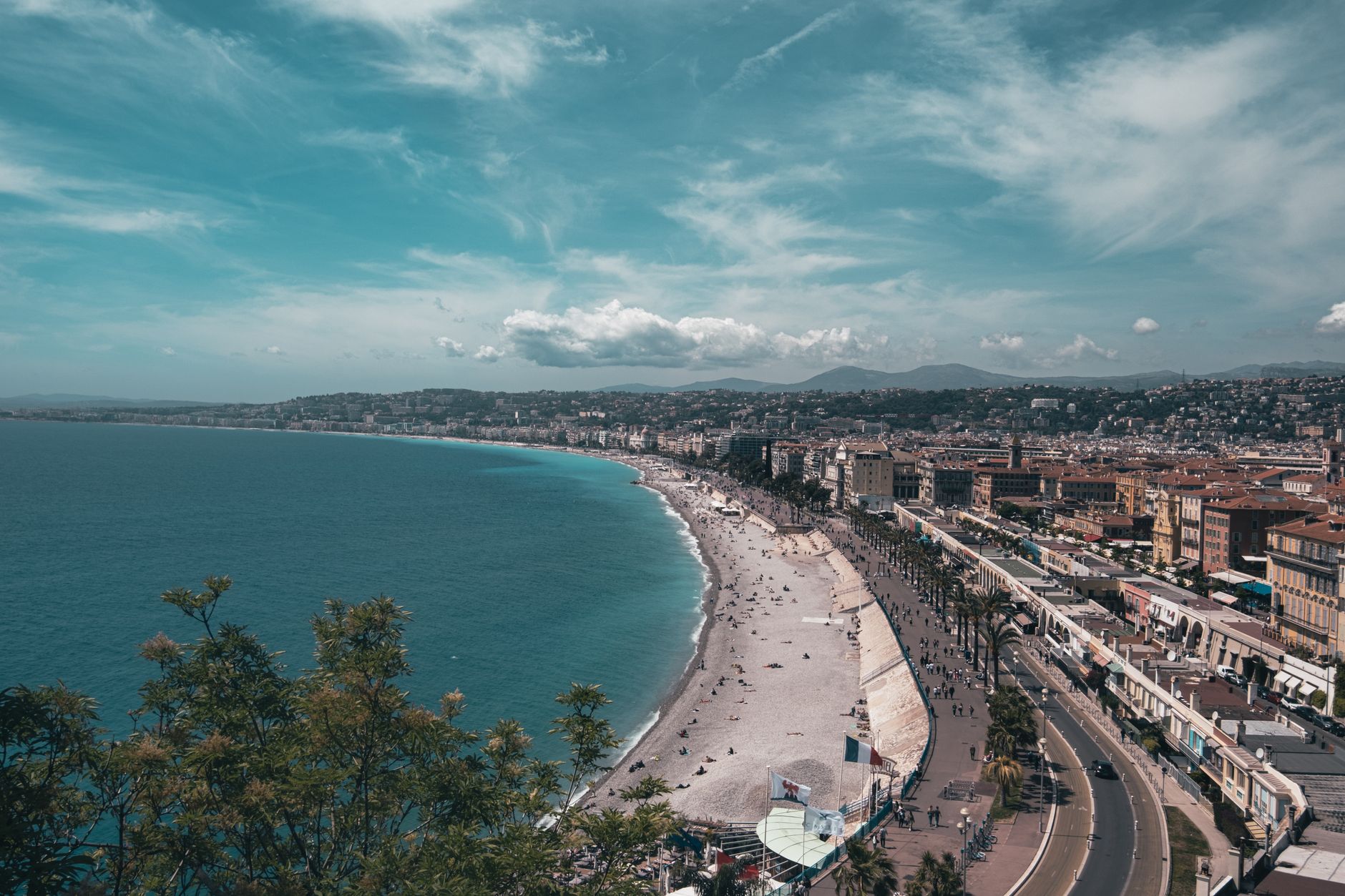 Pohled na pobřeží Nice s azurovým mořem, plážovou promenádou Promenade des Anglais a růžovými střechami starého města
