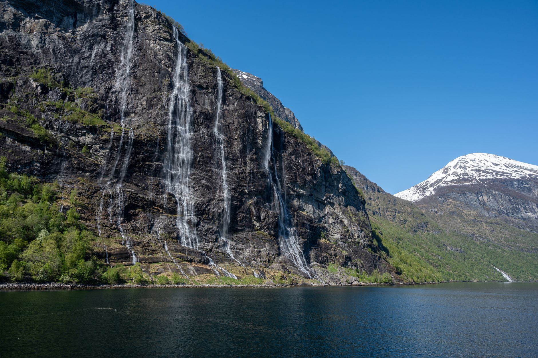 Geirangerfjord v Norsku se strmými útesy a vodopády padajícími do tmavě modré vody fjordu