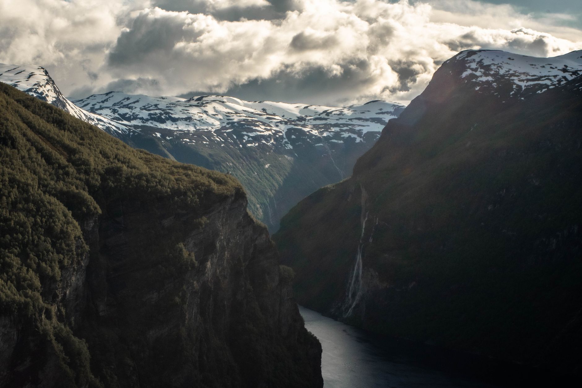Geirangerfjord v Norsku se strmými zelenými útesy a vodopády padajícími do hluboké modré vody