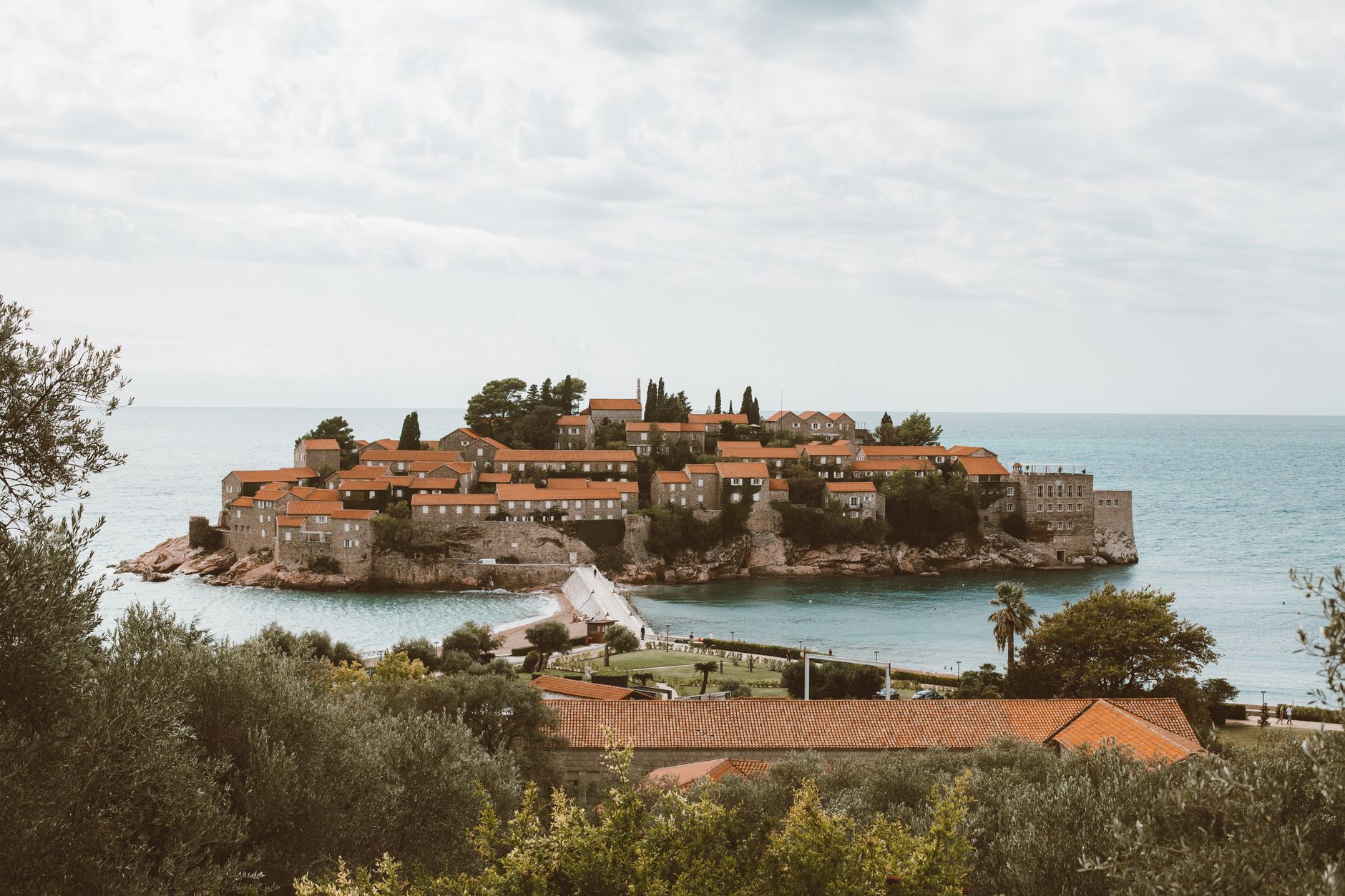 Ostrůvek Sveti Stefan v Černé Hoře spojený úzkou šíjí s pevninou, kamenné domy s červenými střechami