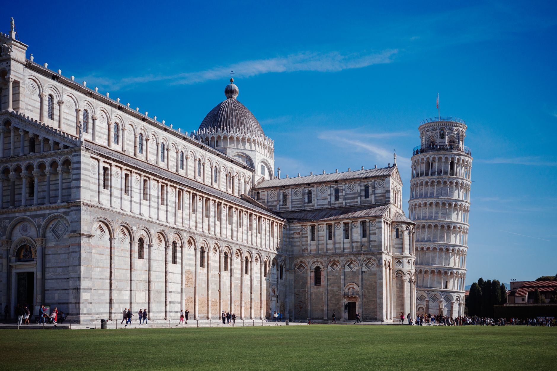 Šikmá věž v Pise a katedrála na zeleném trávníku náměstí Piazza dei Miracoli za jasného dne