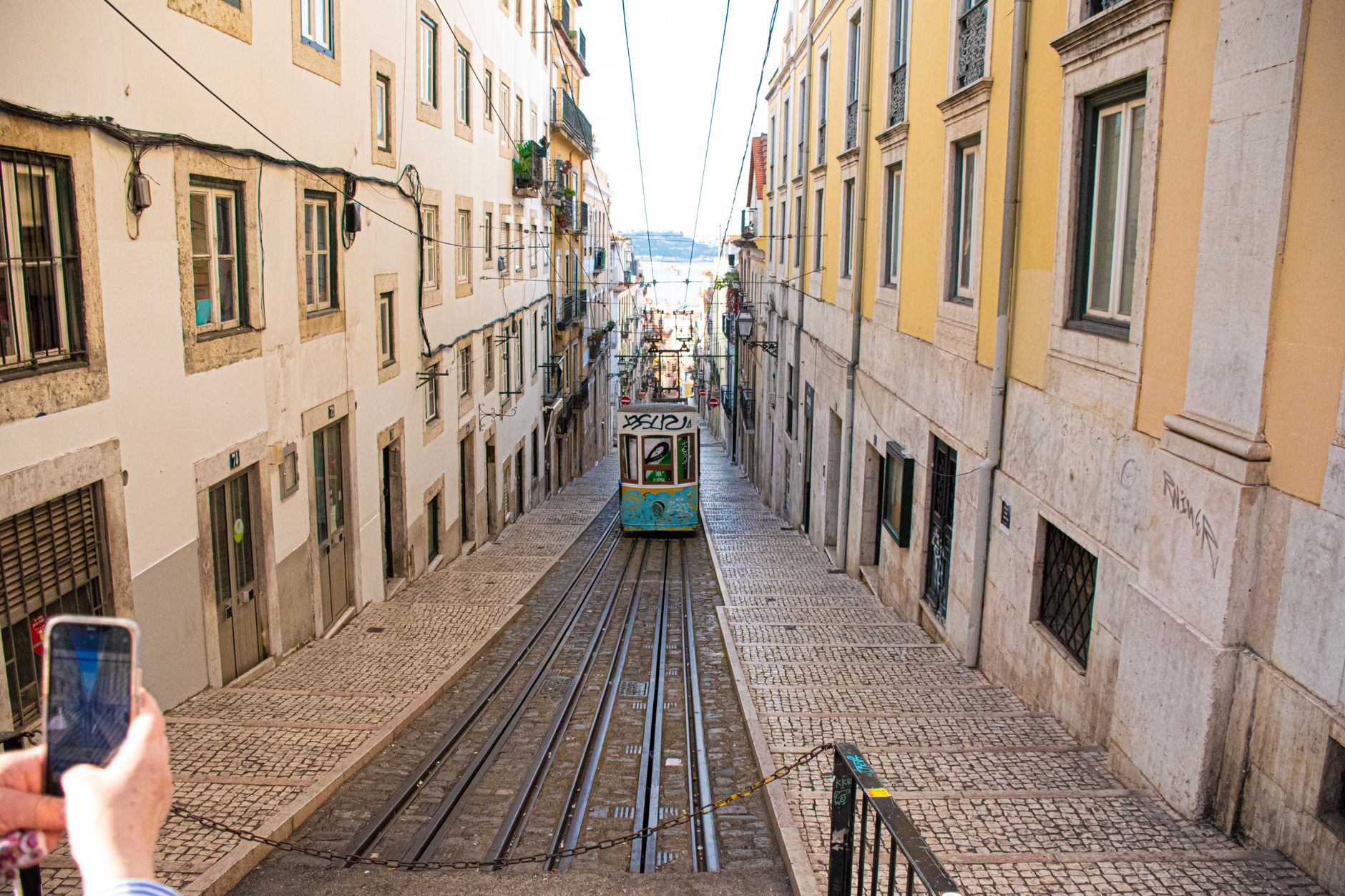 Žlutá historická tramvaj v úzké strmé uličce čtvrti Alfama v Lisabonu