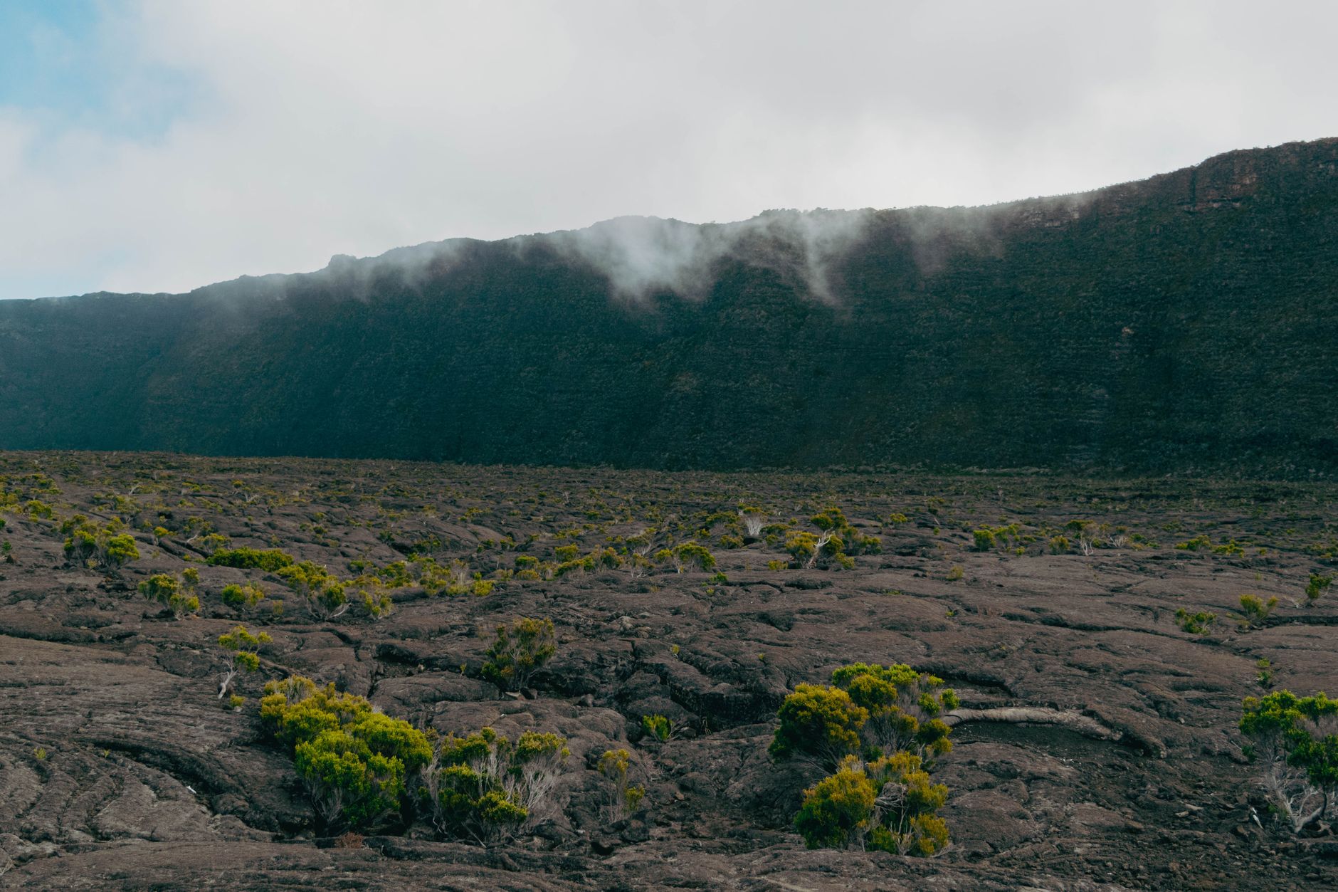 Lávové pole a kráter činné sopky Piton de la Fournaise na ostrově Réunion pod modrou oblohou