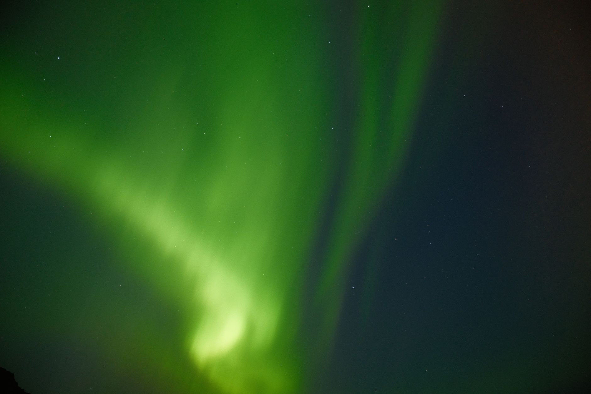 Polární záře nad krajinou na Islandu, zelené pruhy aurory na noční obloze