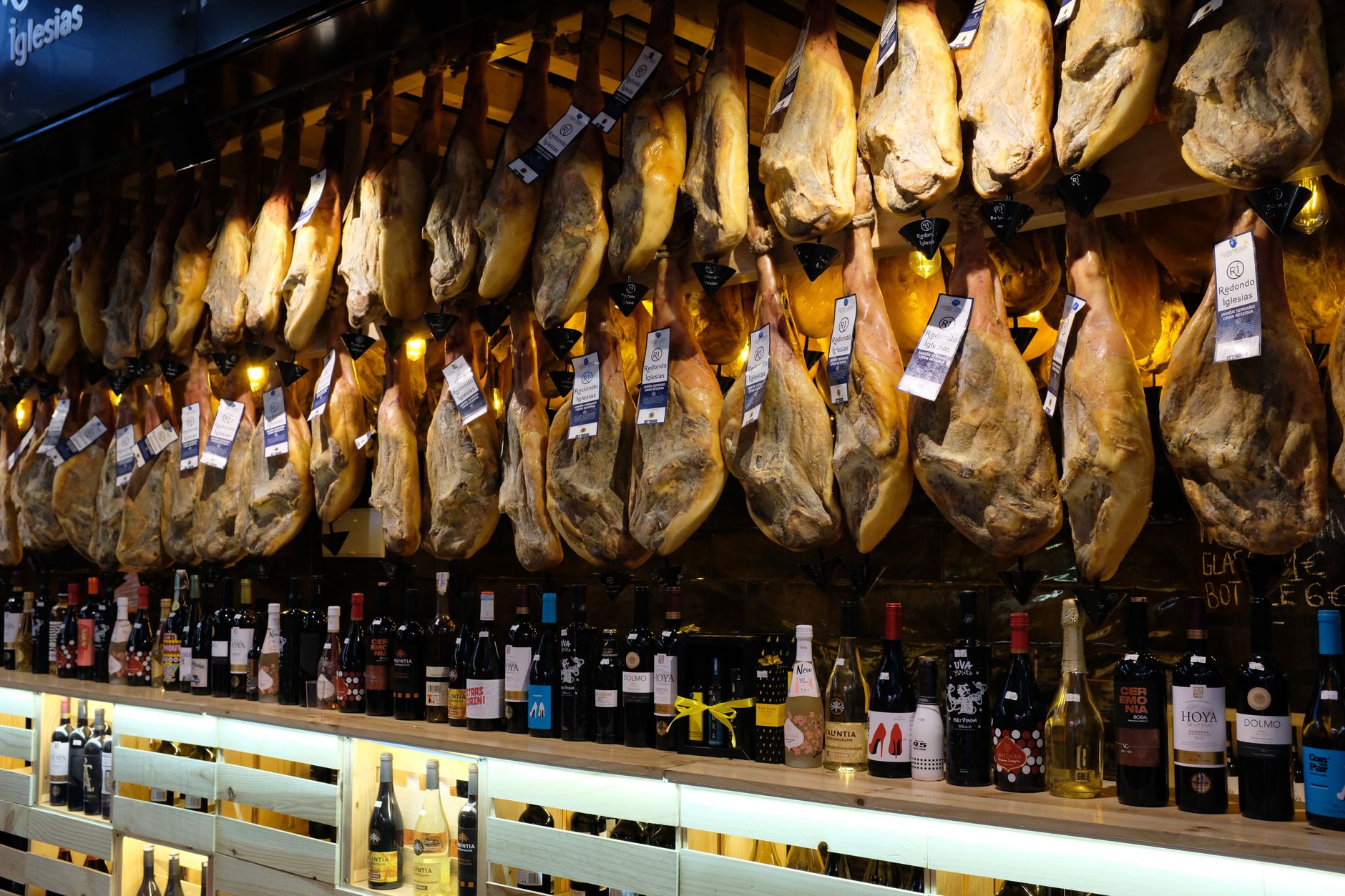 Talíř španělských tapas s jamónem a chlebem vedle sklenky červeného vína na stole