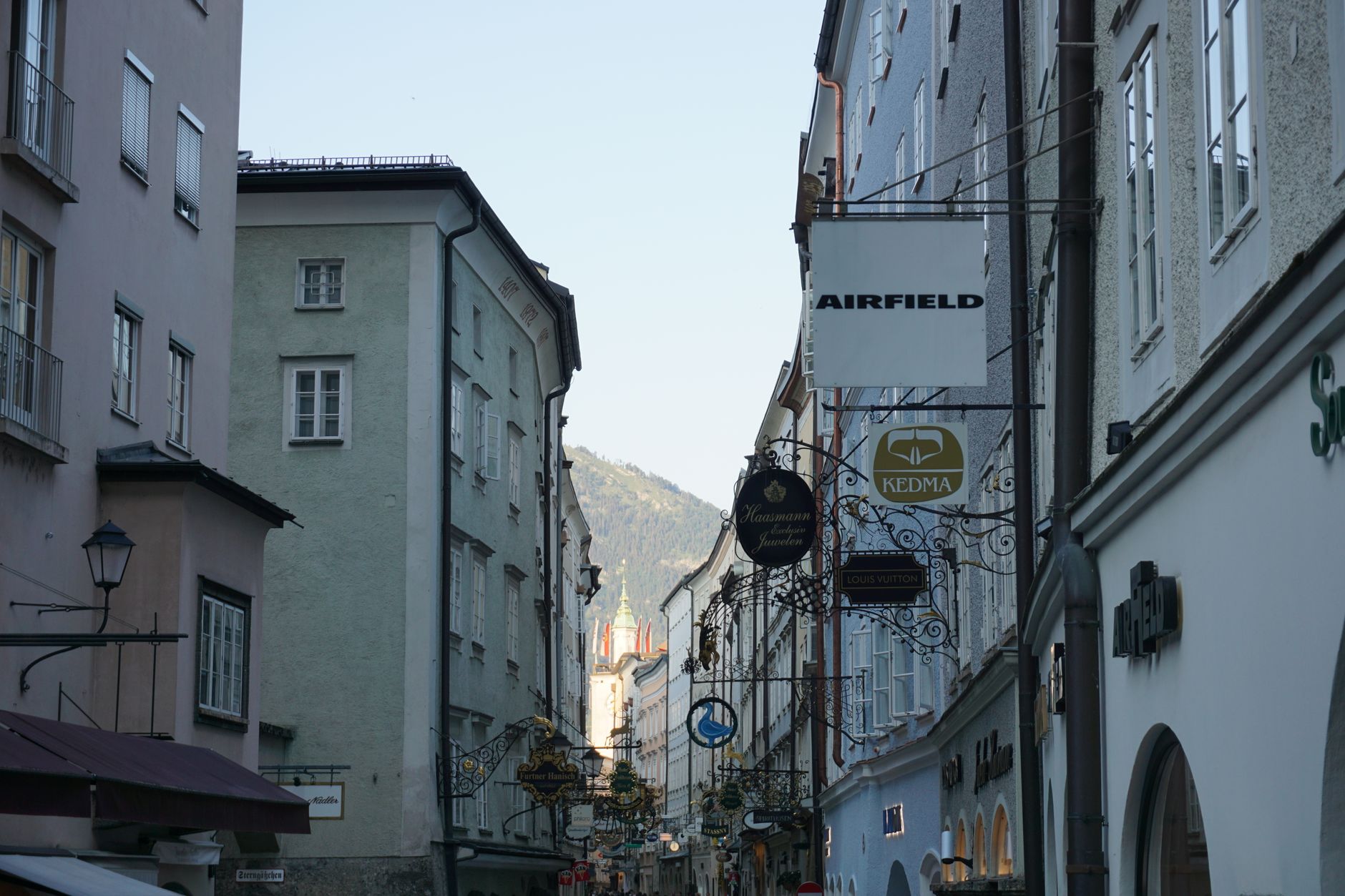 Úzká ulice Getreidegasse v Salzburgu s historickými kovanými cechovními štíty nad obchody