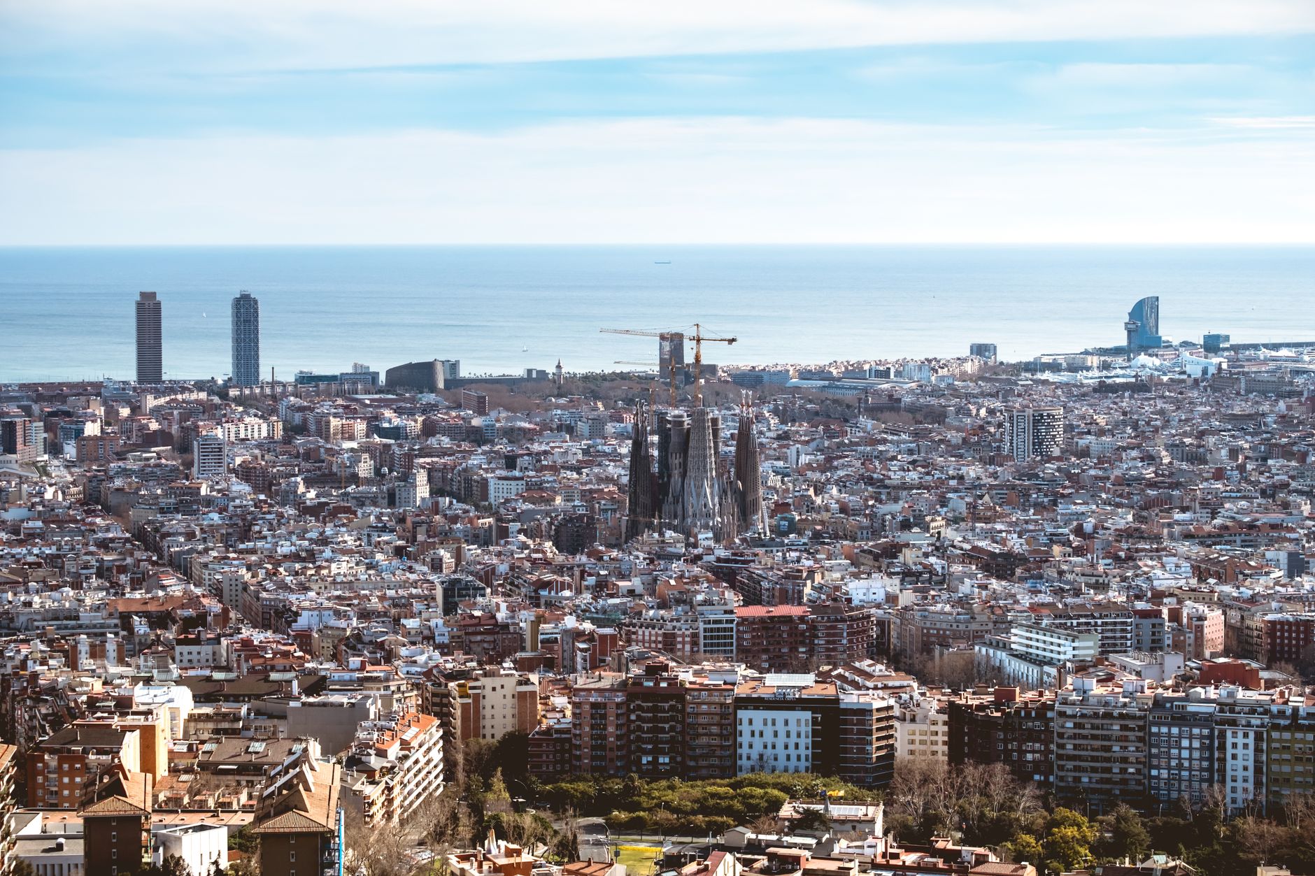 Panoramatický pohled na chrám Sagrada Família a střechy Barcelony s horami v pozadí