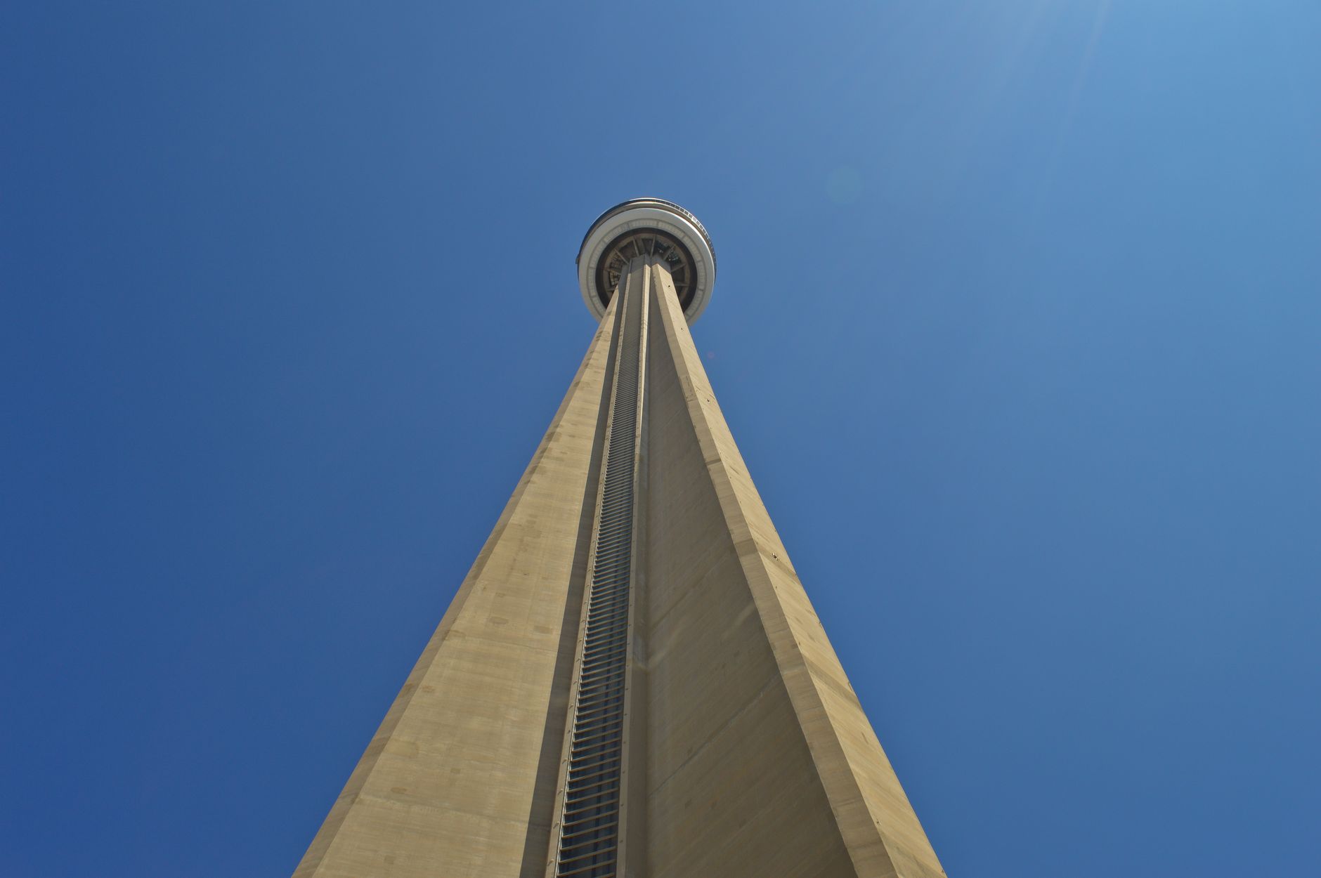 Věž CN Tower v Torontu zdola pohledem na prosklenou vyhlídkovou plošinu proti modré obloze